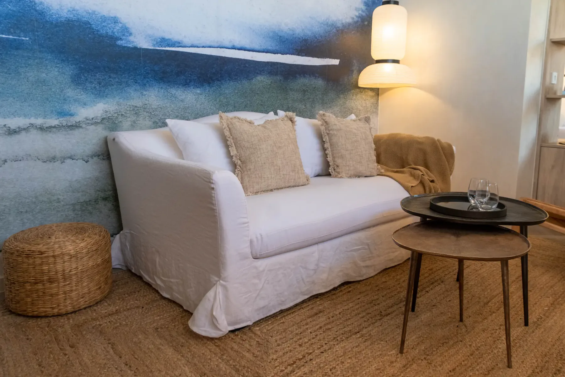 A living room with a white sofa, round tables, and a large wall mural.