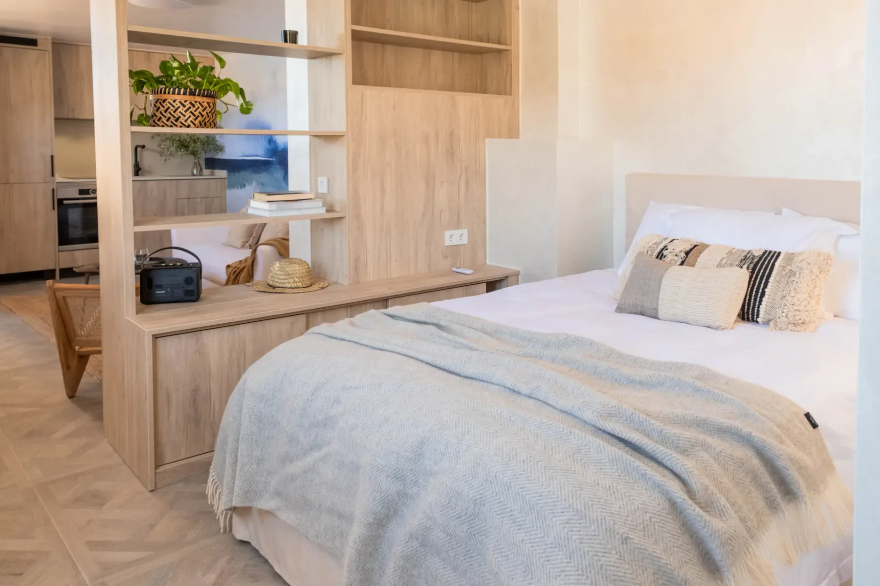 A bright bedroom with a neatly made bed and built-in wooden shelving.