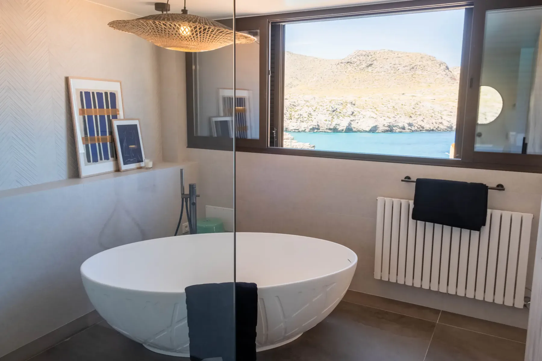 A bright bathroom with a freestanding bathtub beside a wide window overlooking the water.