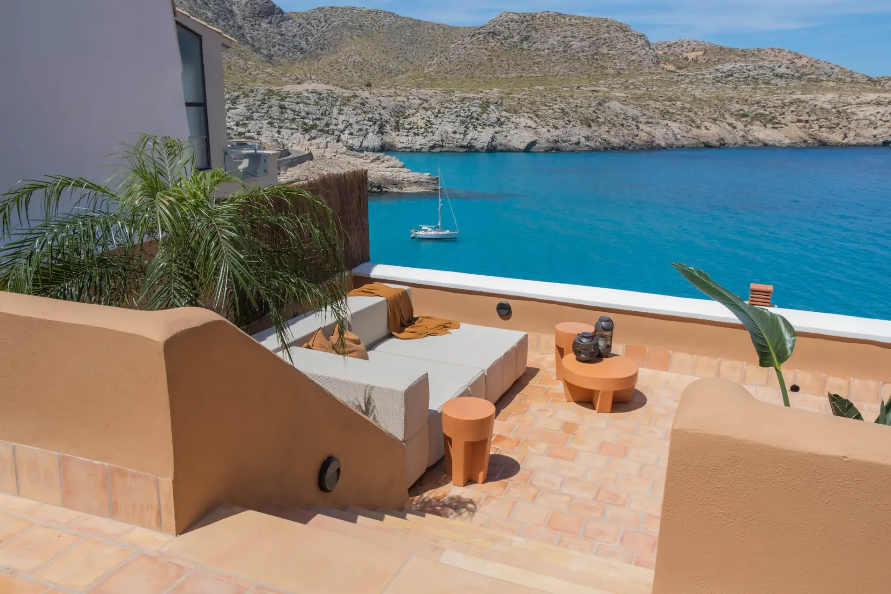 A sunny terrace overlooks turquoise water and a rocky coastline.