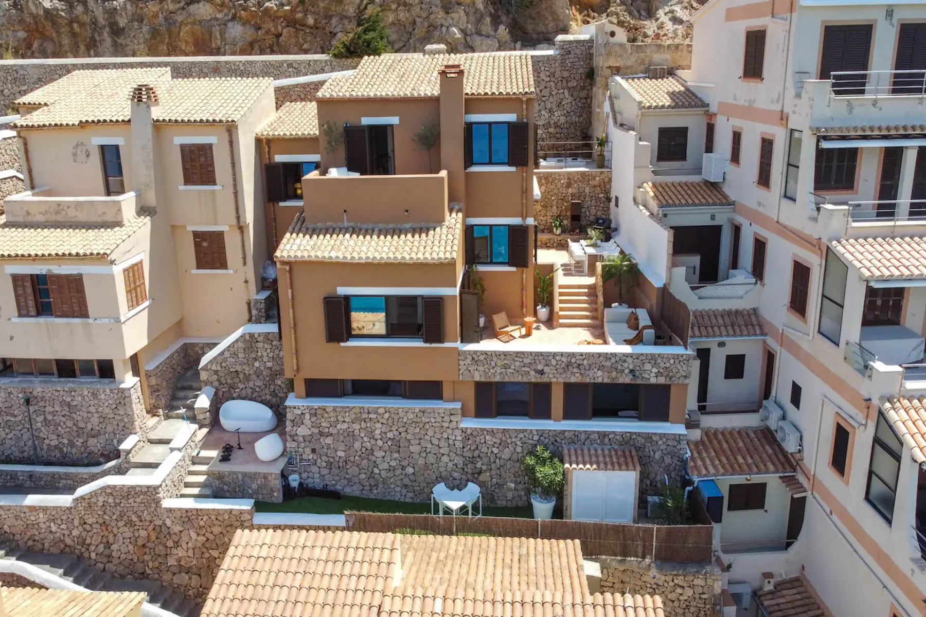 Aerial view of closely spaced homes with tiled roofs and stone retaining walls.