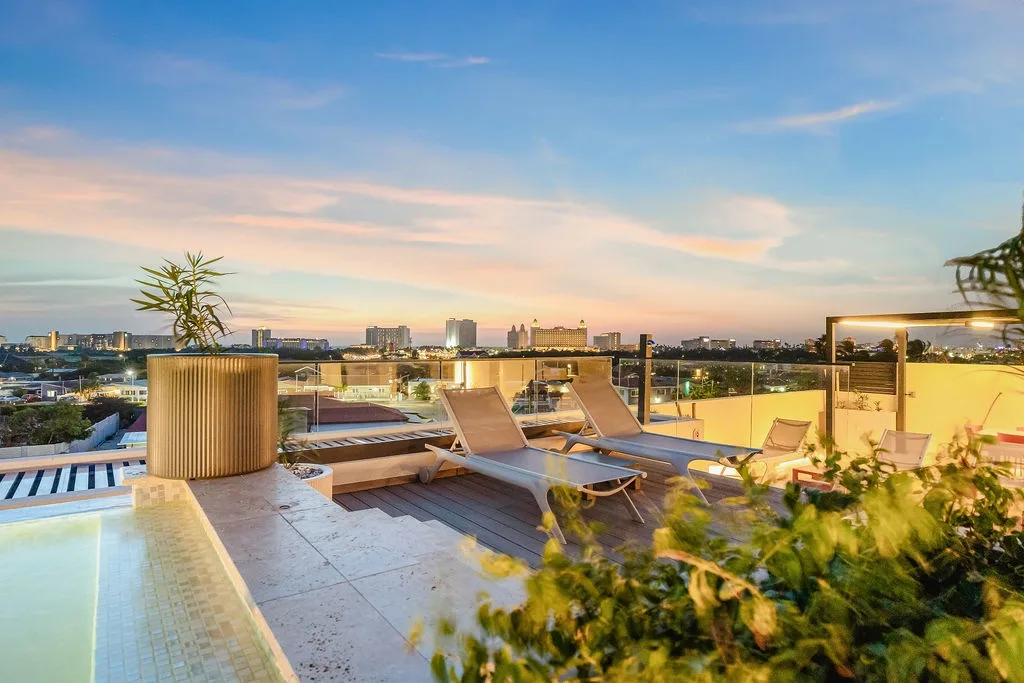 Rooftop terrace captures the urban skyline at golden hour, with lounge chairs and greenery overlooking the surrounding cityscape.