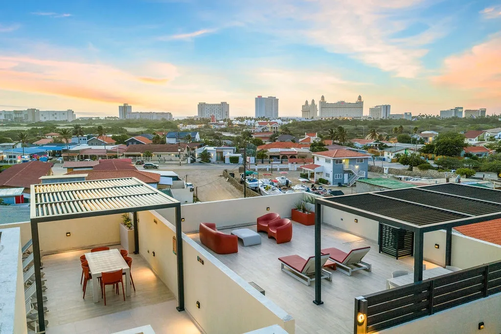 Panoramic rooftop terrace featuring shaded dining and multiple lounging areas overlooking the coastal cityscape at golden hour.