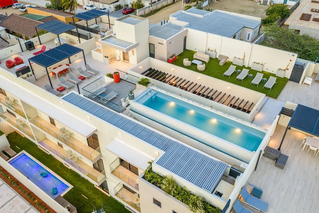 An aerial view capturing the modern architecture and expansive rooftop amenities, including a stunning pool and multiple lounge areas perfect for sunny days and starry nights.