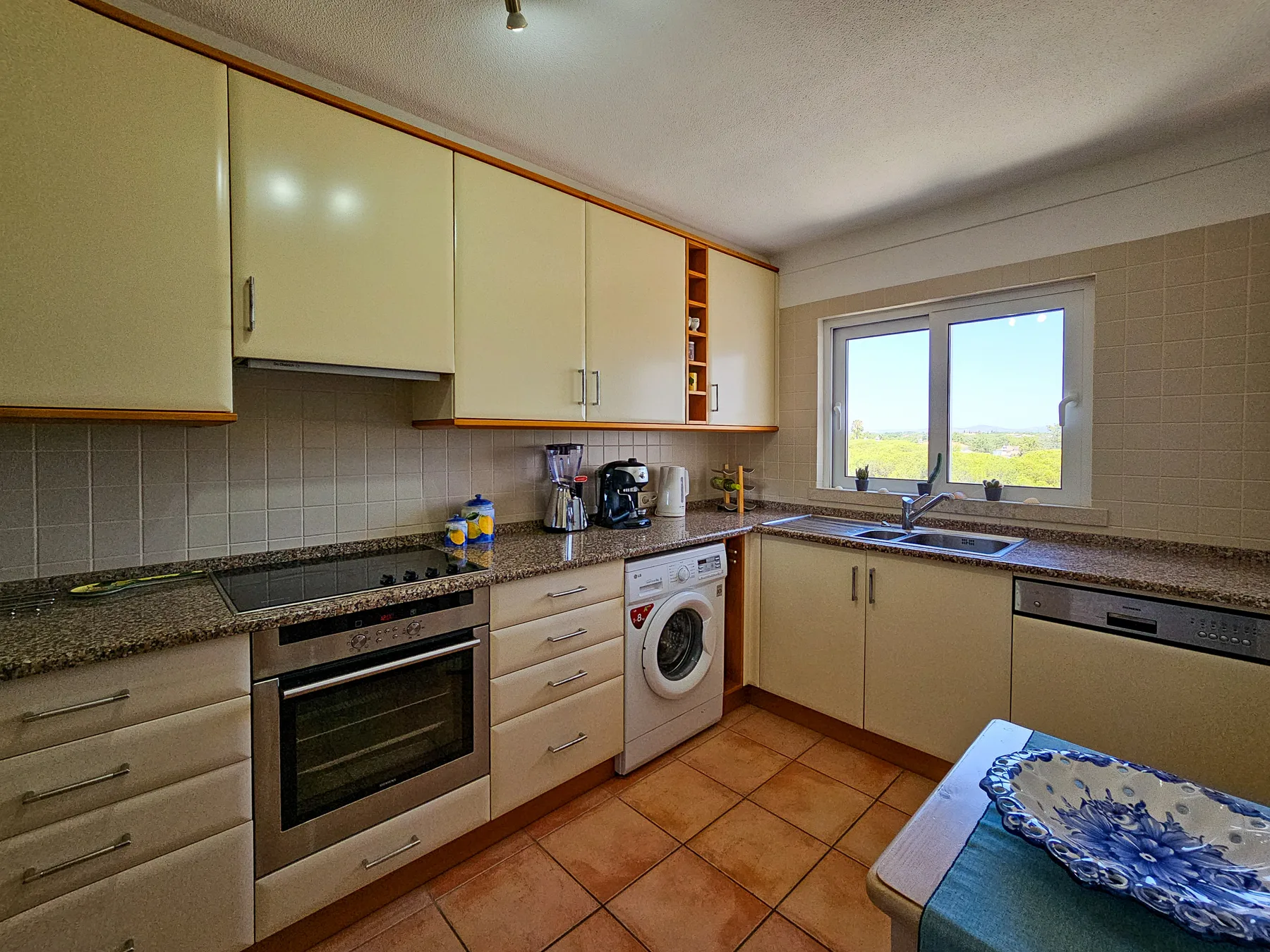 Cocina con armarios claros, un salpicadero de azulejos y una ventana sobre la encimera.