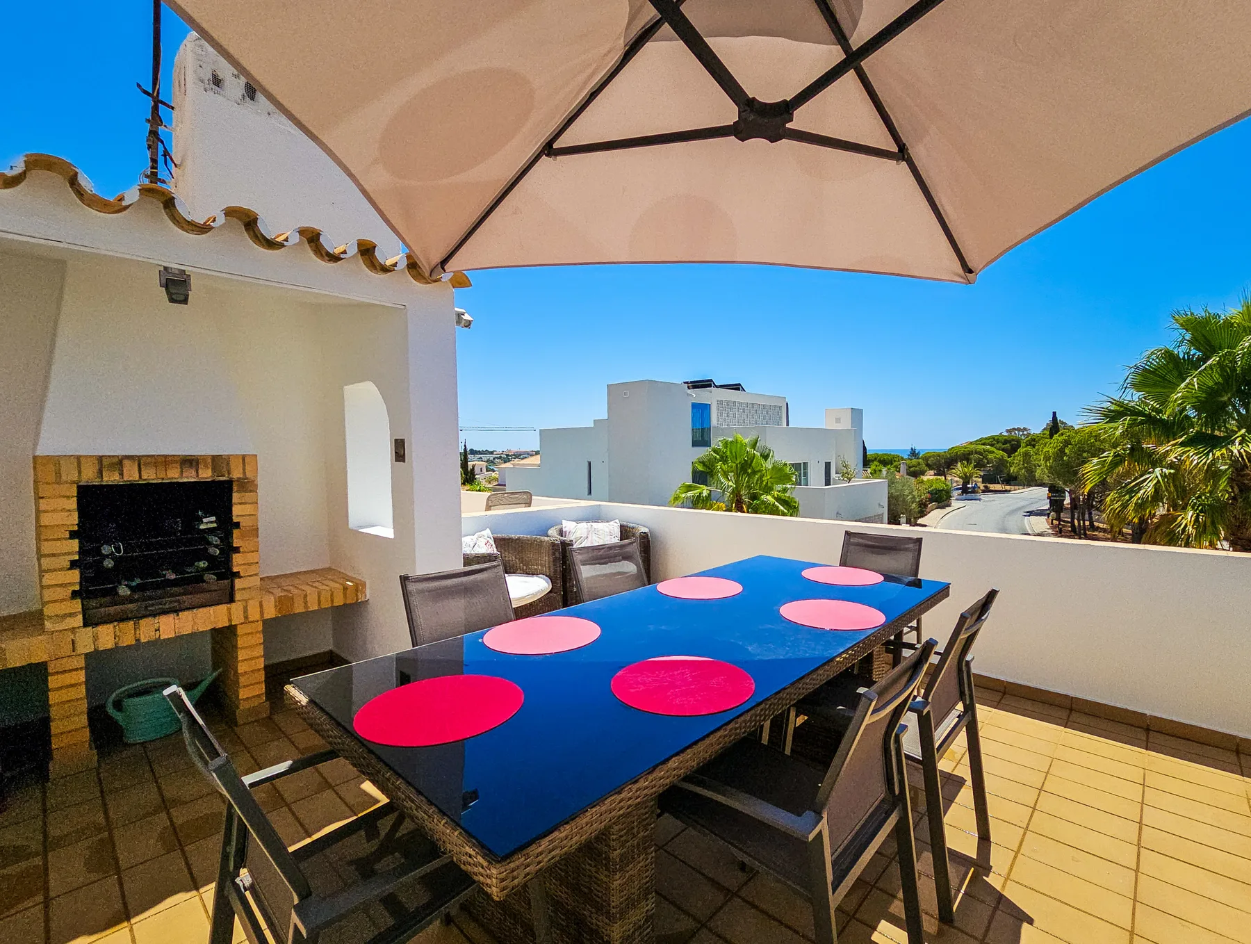 Comedor exterior soleado con una mesa colorida, asientos y una barbacoa de obra.