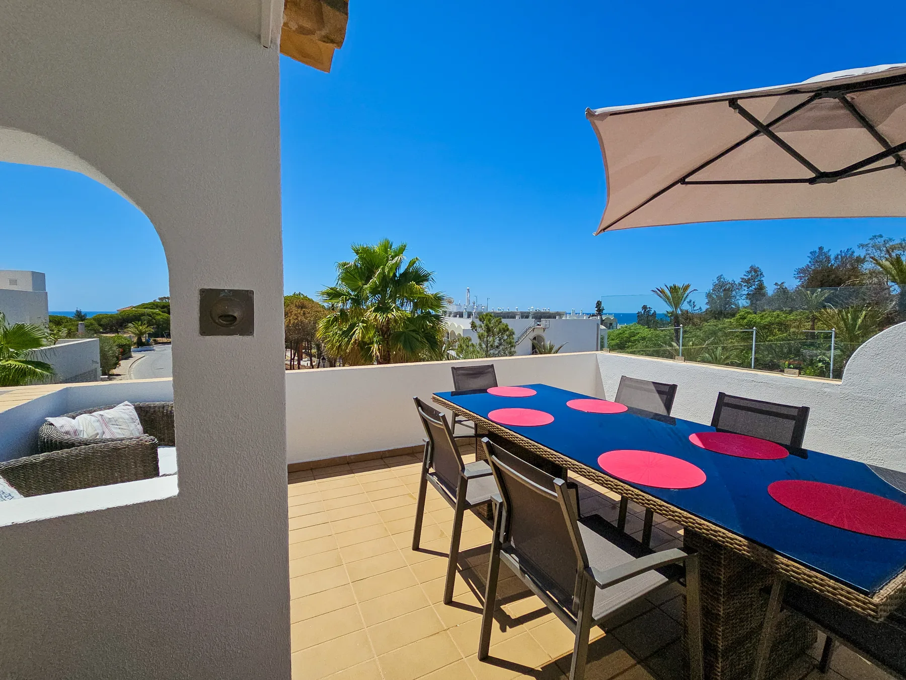 A sunny terrace dining area with a long table and outdoor seating.