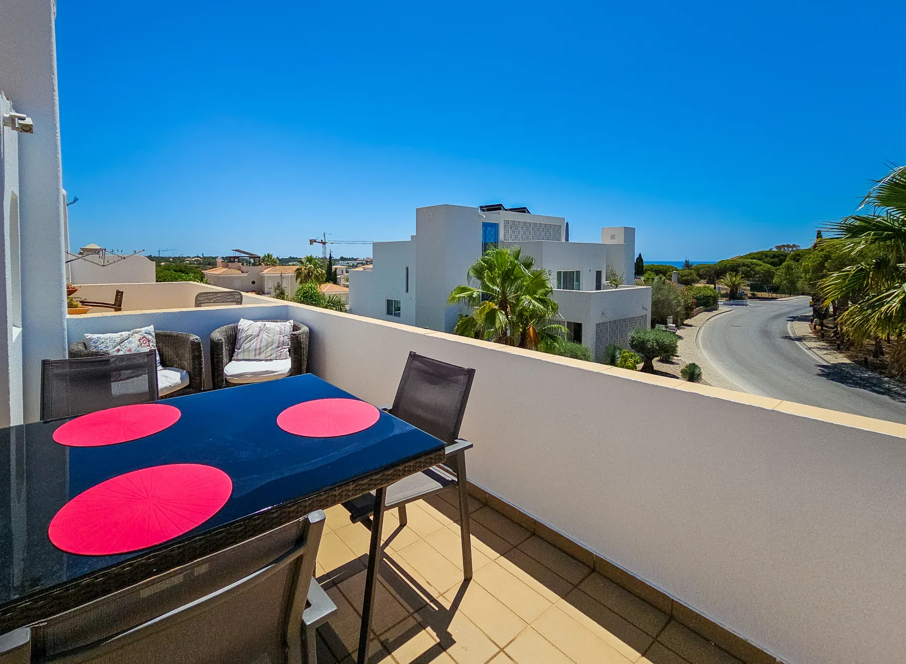 A sunny terrace with outdoor seating overlooks nearby buildings and a curving road.