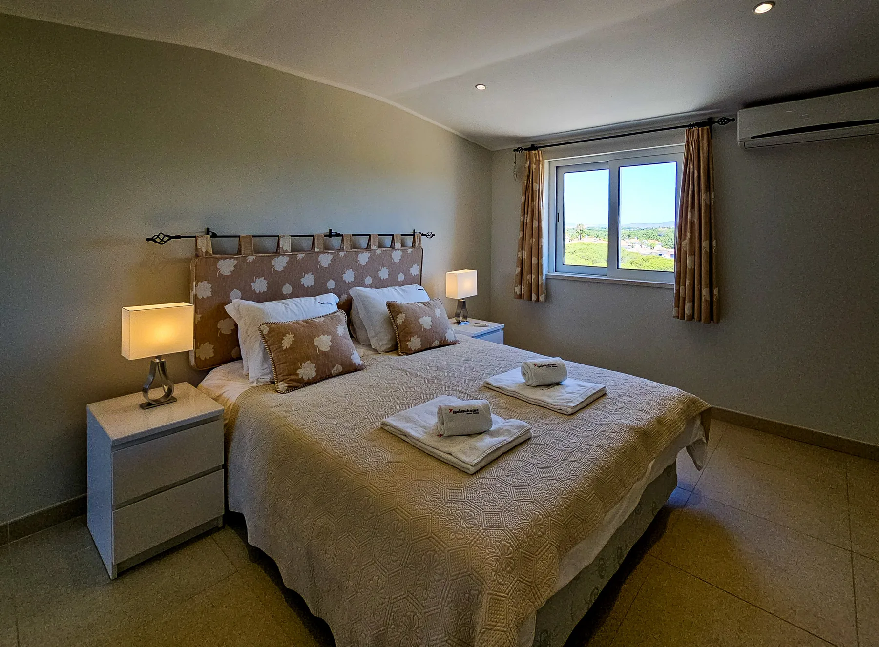 Un dormitorio con cama doble, mesitas de noche y una ventana con vistas a zonas verdes.