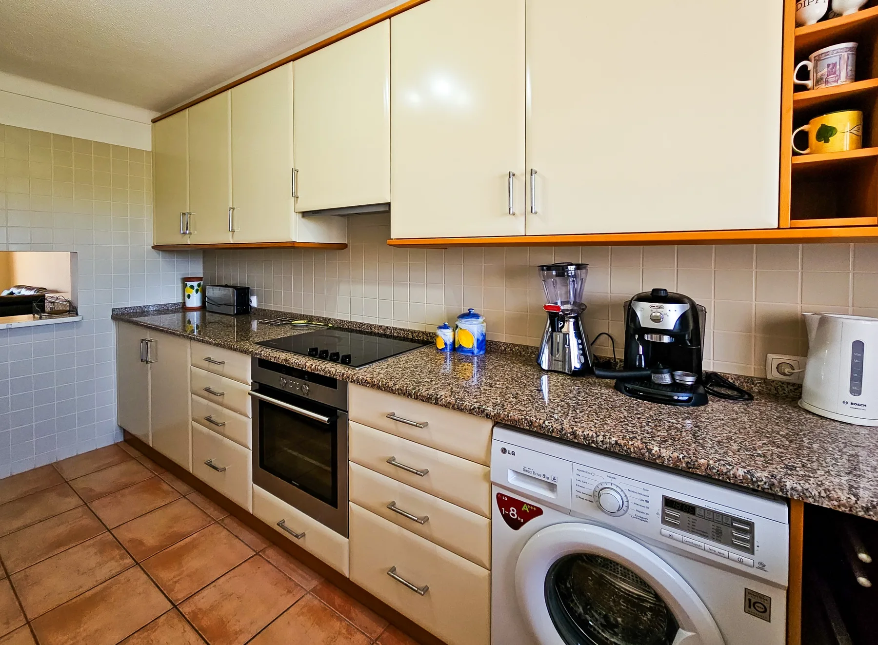 Una cocina equipada con una placa de cocción y pequeños electrodomésticos sobre la encimera.