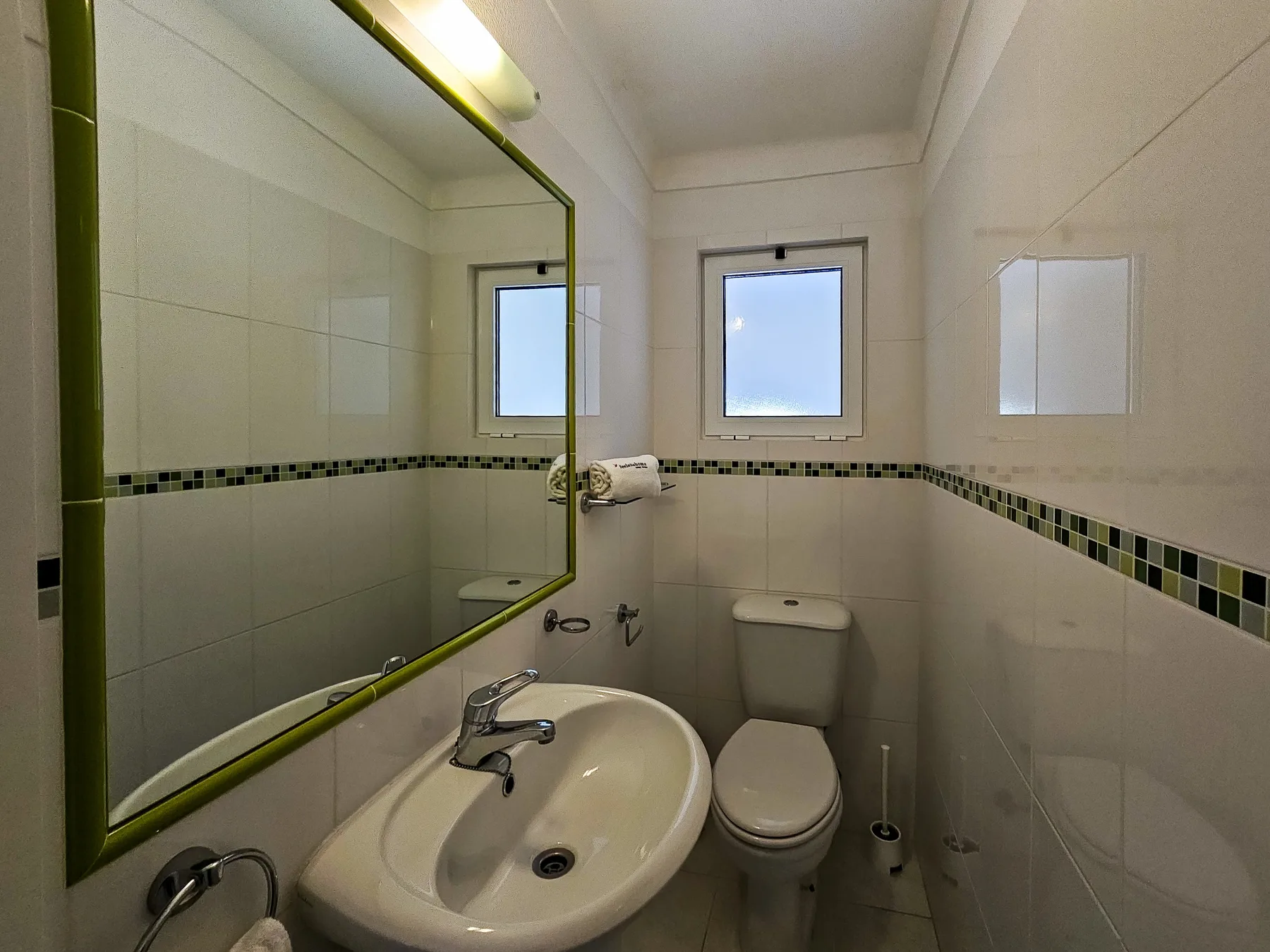 Un baño alicatado con lavabo, inodoro y ventanas pequeñas.