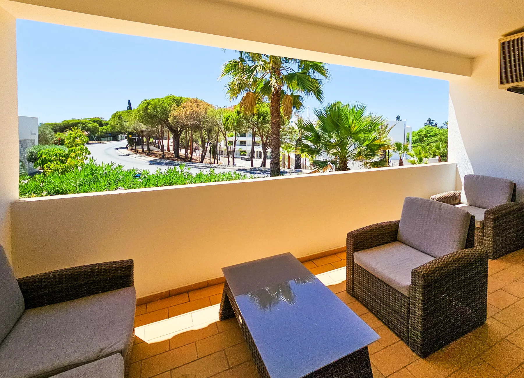 Una terraza cubierta con asientos acolchados da a palmeras y vegetación.