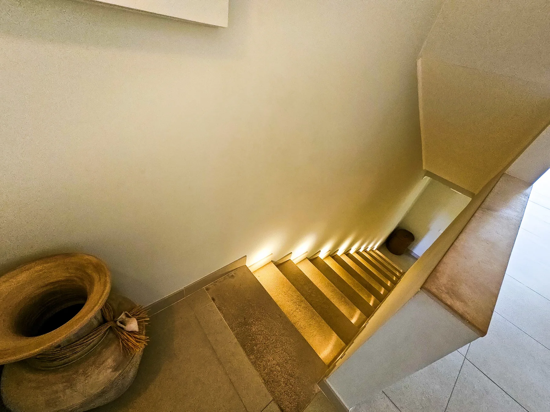 An indoor staircase descends beside a large decorative pot.