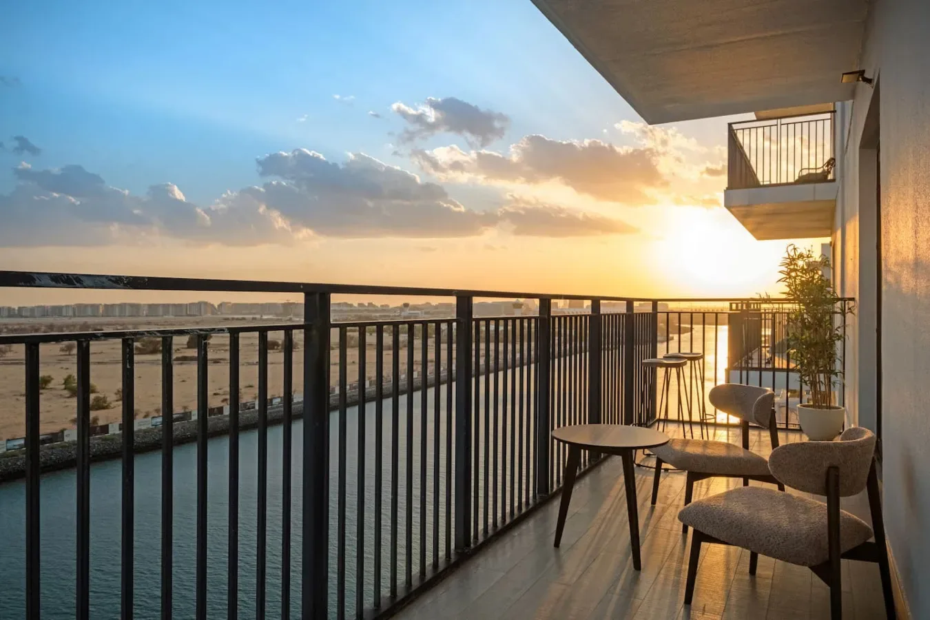A balcony with seating overlooks the water at sunset.