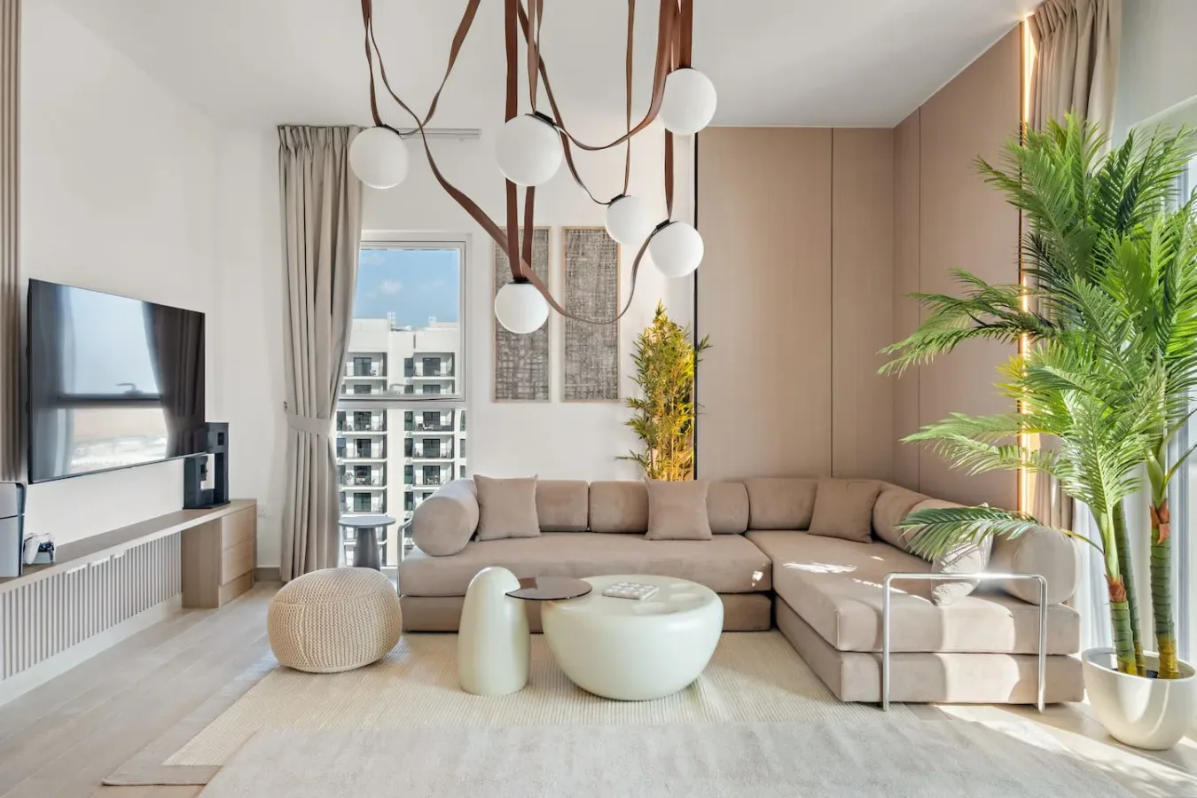 A bright living room with a sectional seating area, round tables, and tall plants.