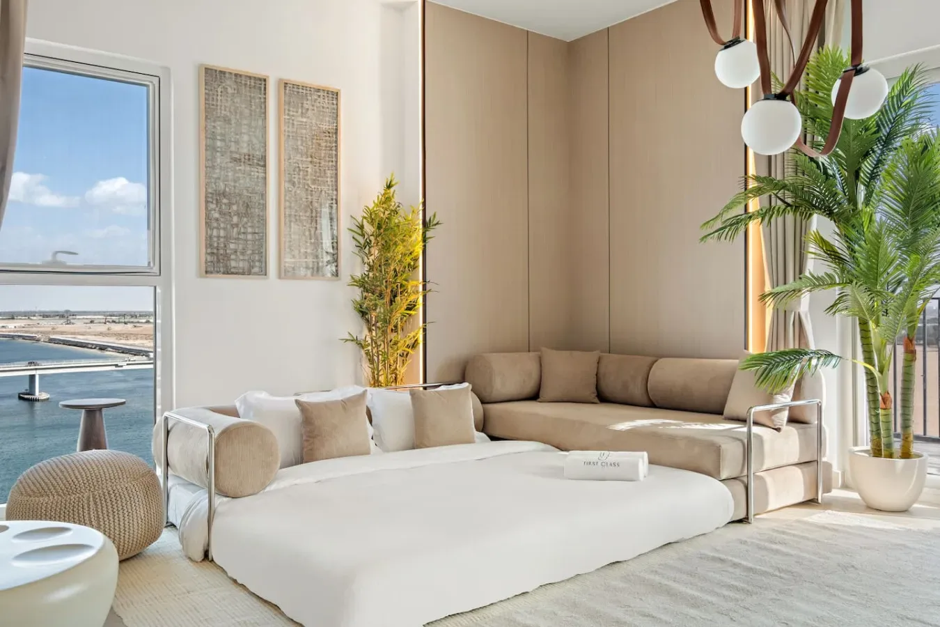 Una sala luminosa con una cama blanca grande y una zona de asientos beige junto a la ventana.