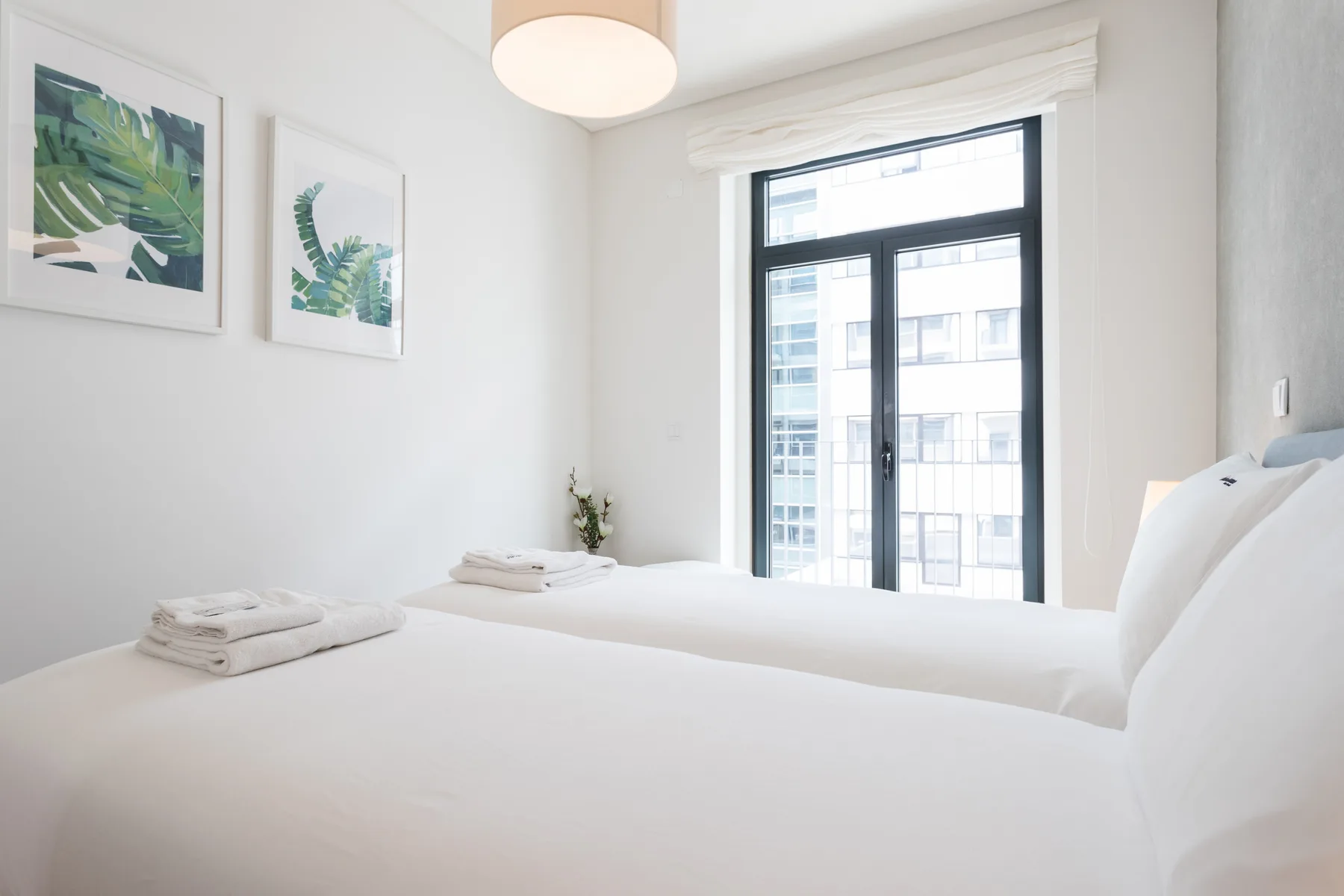 Un dormitorio luminoso con ropa de cama blanca y láminas botánicas enmarcadas.