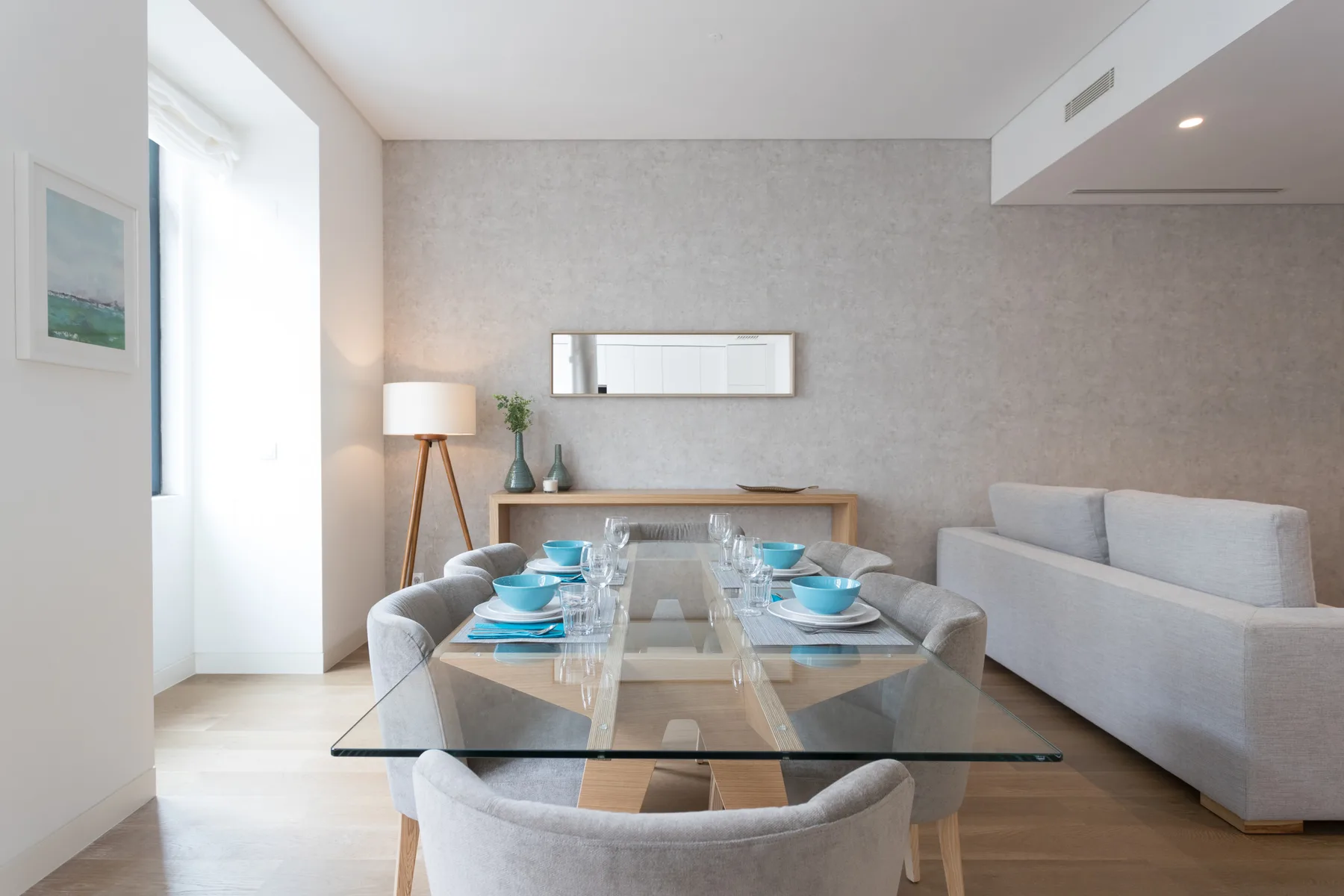 Un comedor moderno con una mesa de vidrio y asientos tapizados junto a una sala de estar.