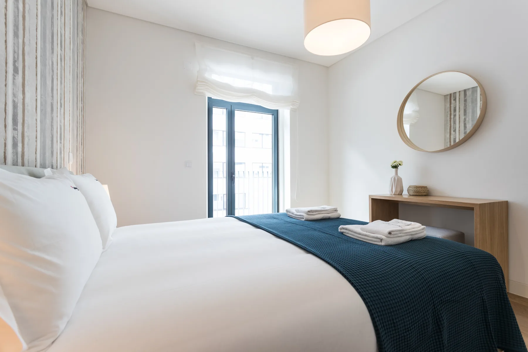 Un dormitorio luminoso con ropa de cama blanca y una colcha azul.