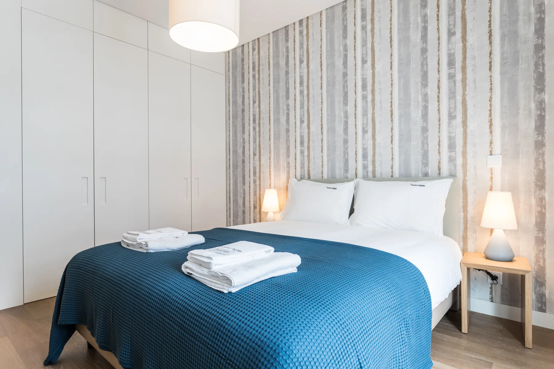 Un dormitorio con una cama vestida con una colcha azul y sábanas blancas.
