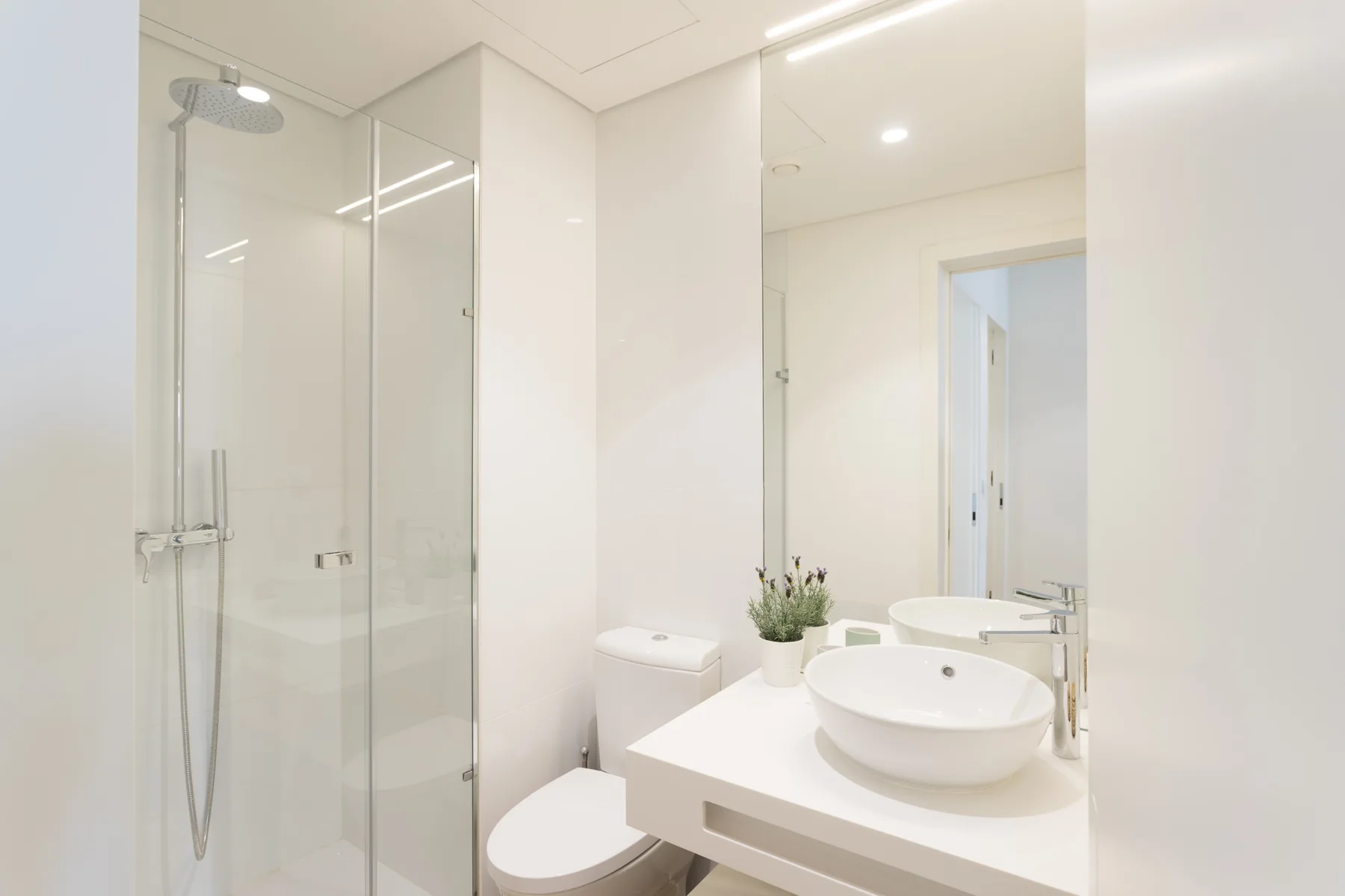 Un baño luminoso con una ducha de vidrio y un lavabo blanco.