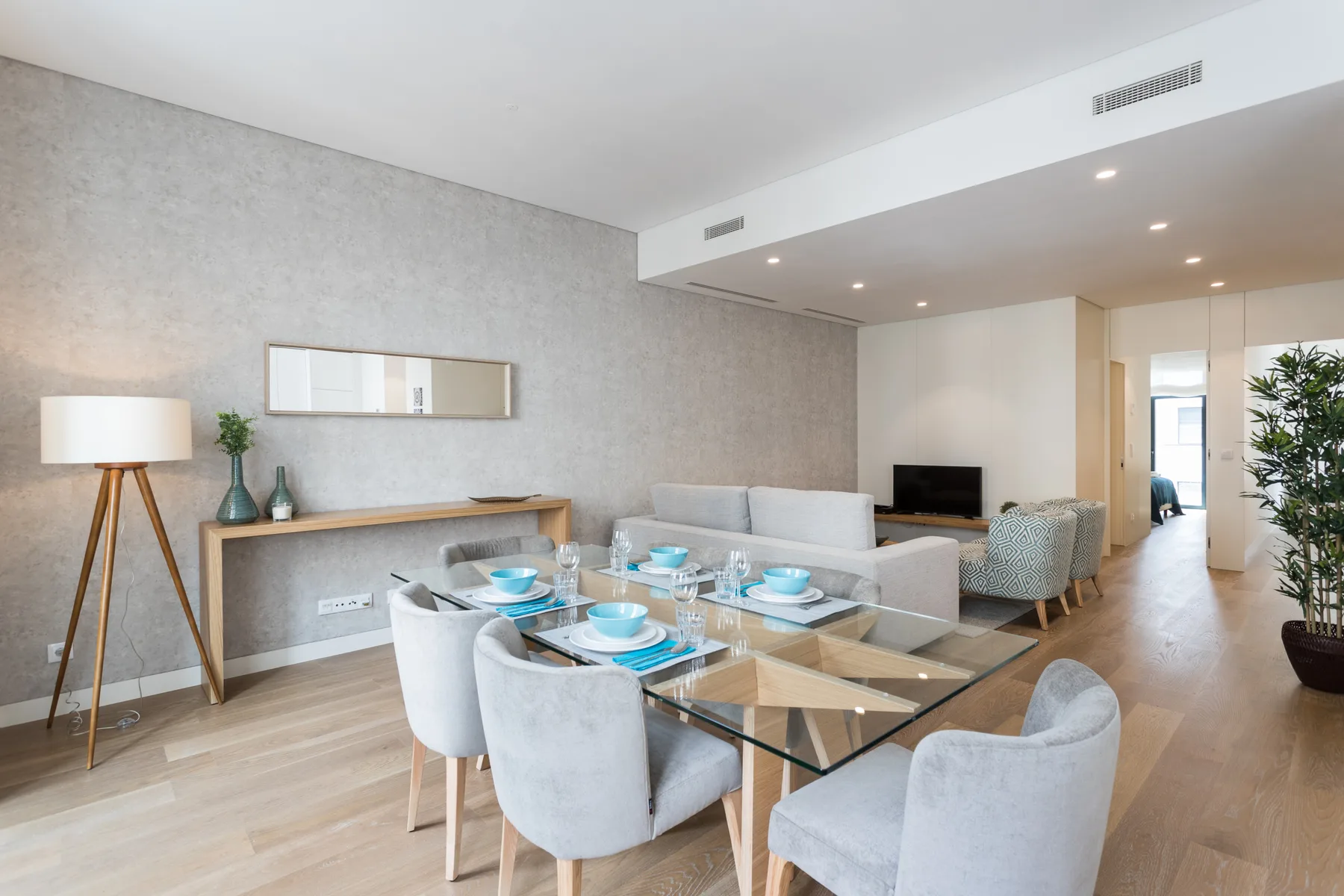 Zona de comedor y estar con una mesa de cristal y asientos de tonos claros.