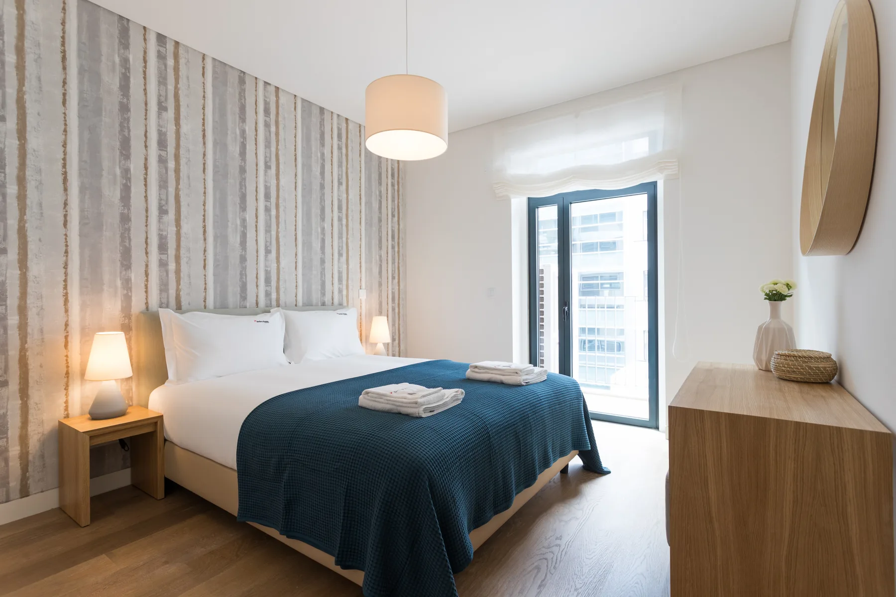 Un dormitorio luminoso con una cama, ropa de cama azul y una ventana grande.