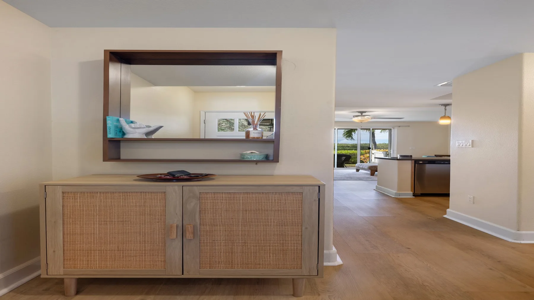 Una sala de estar luminosa y abierta, con un mueble de frente tejido bajo un gran espejo.