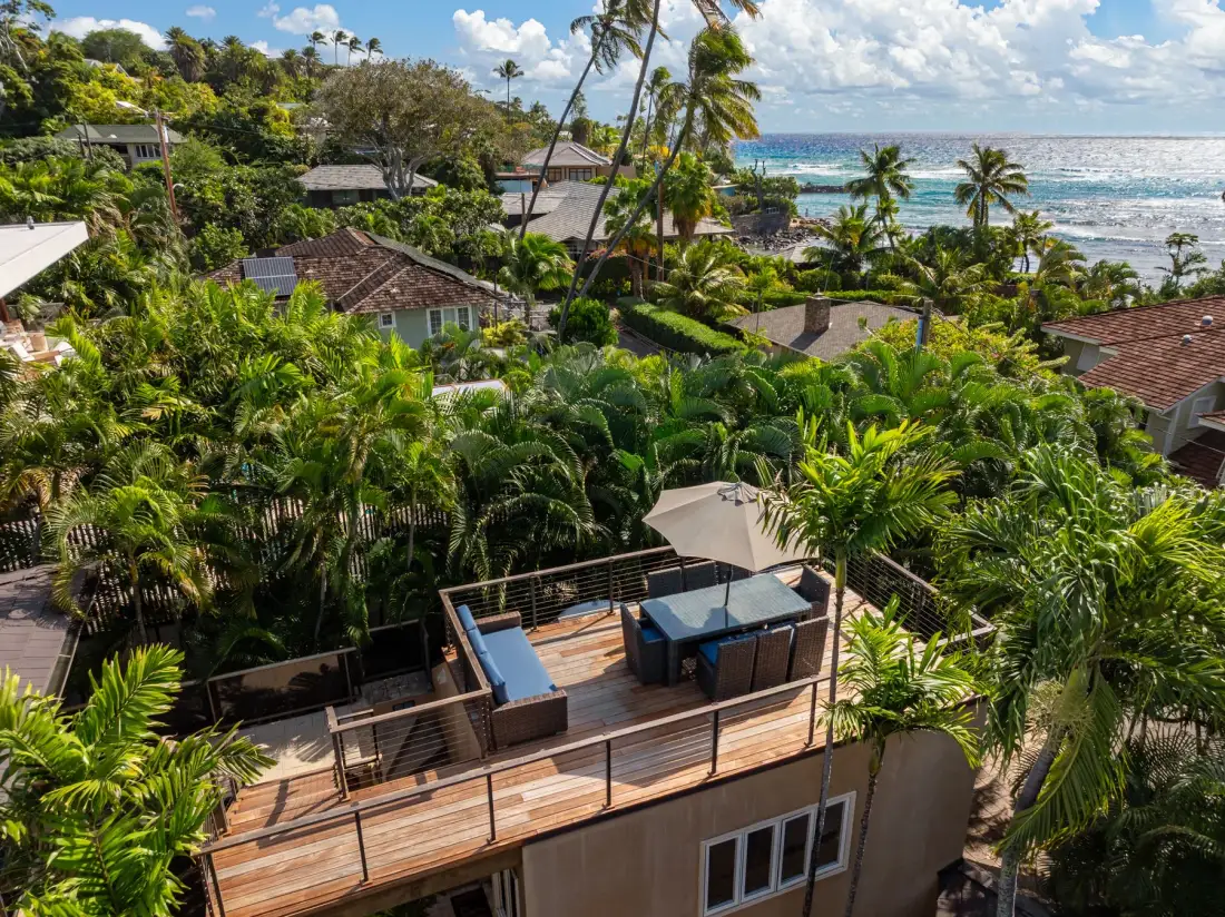 A tropical resort overlooks the ocean, with a furnished terrace in the foreground.