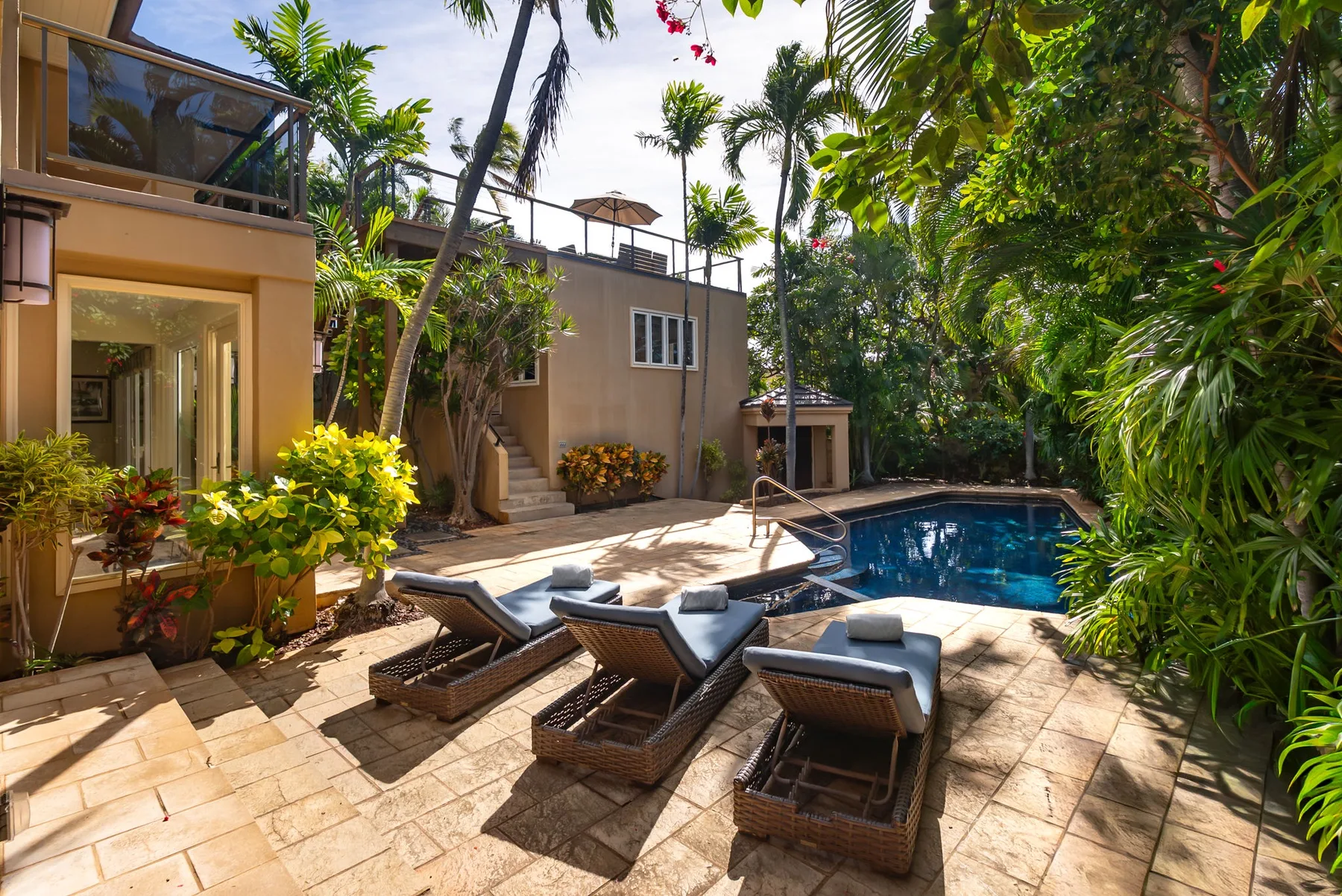 A sunny poolside patio with lounge seating and lush tropical greenery.
