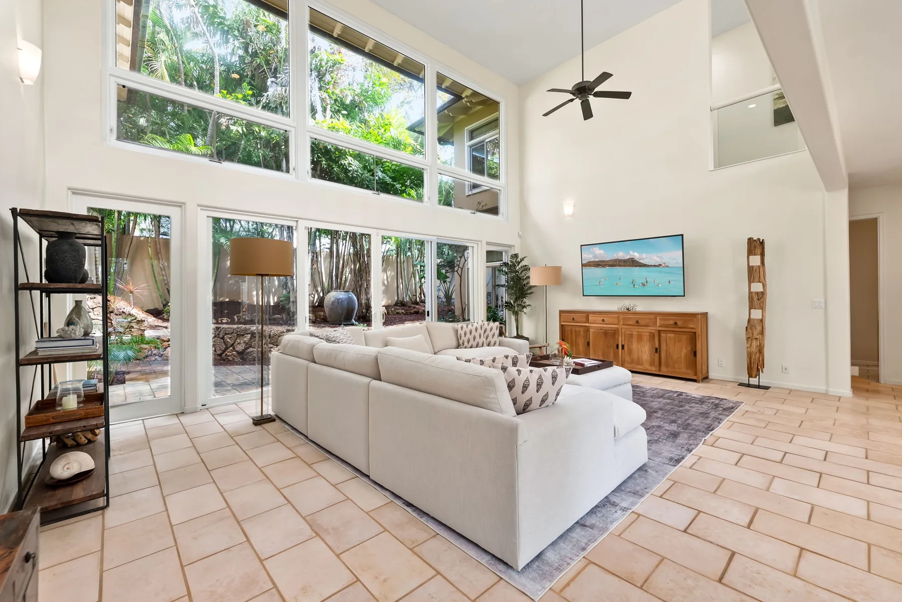 A bright living room with large windows, seating, and a television.