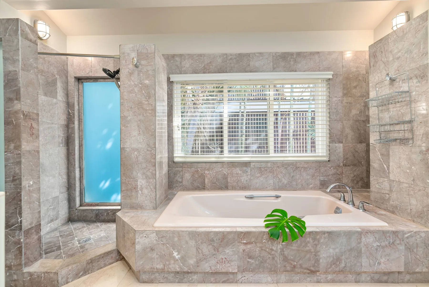 A tiled bathroom with a bathtub beneath a window and a glass shower area.