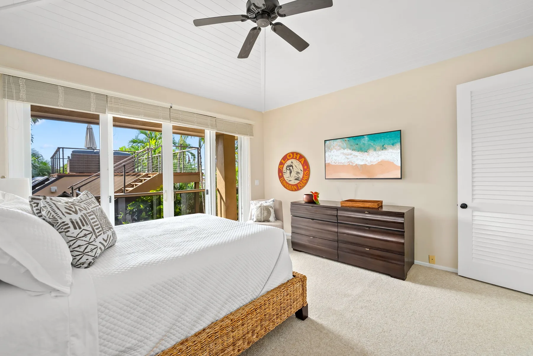 A bright bedroom with a bed beside large windows and a dark dresser.
