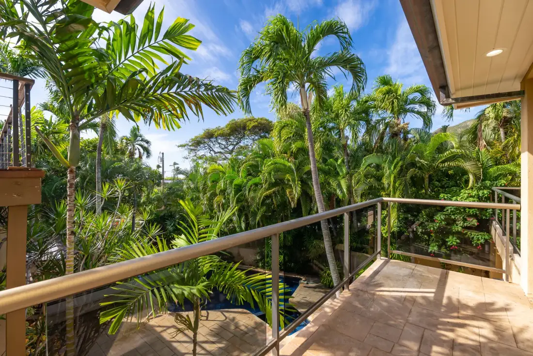 A sunlit outdoor balcony overlooks a lush tropical garden.