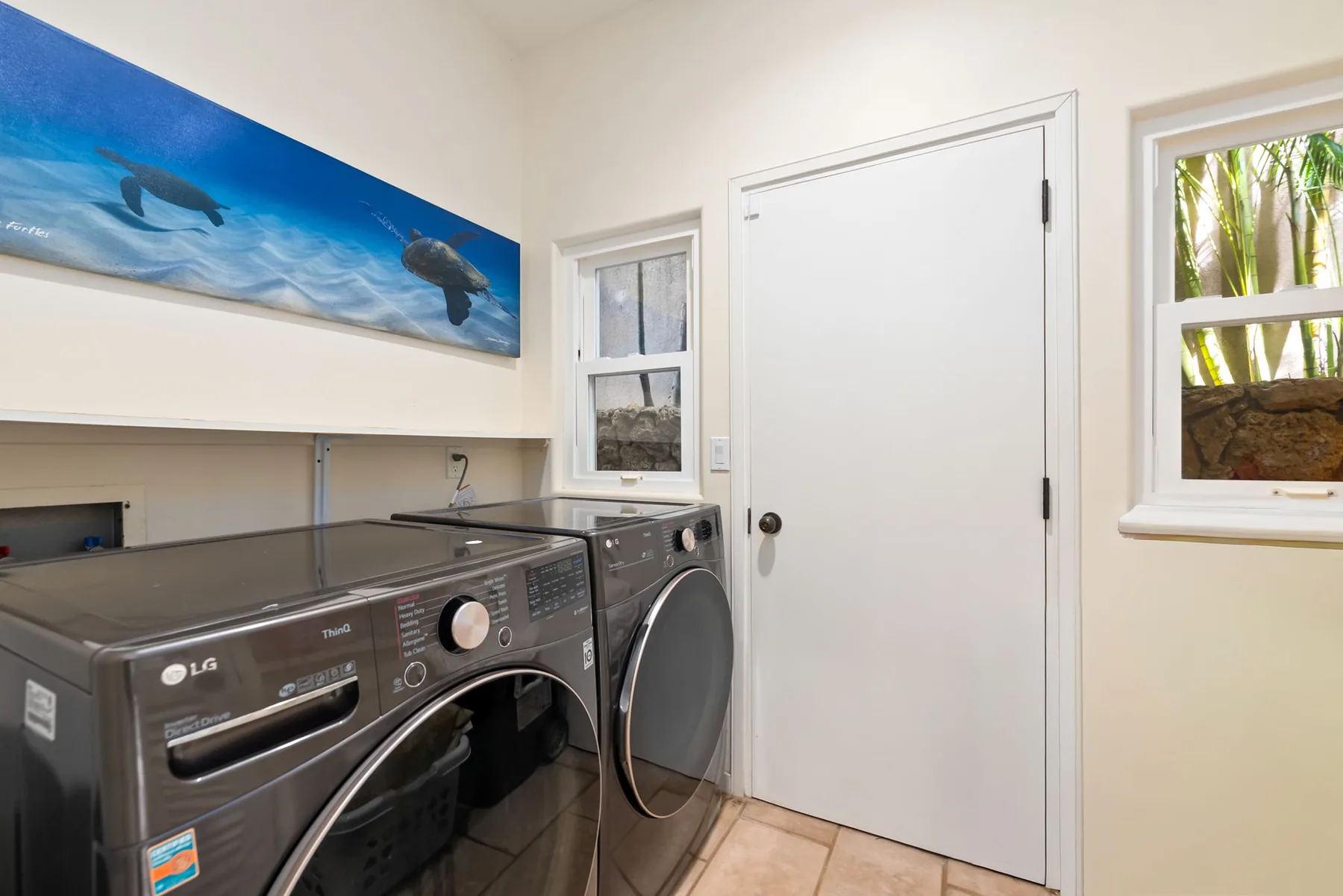 A laundry room with front-loading washer and dryer beneath an ocean-themed wall mural.