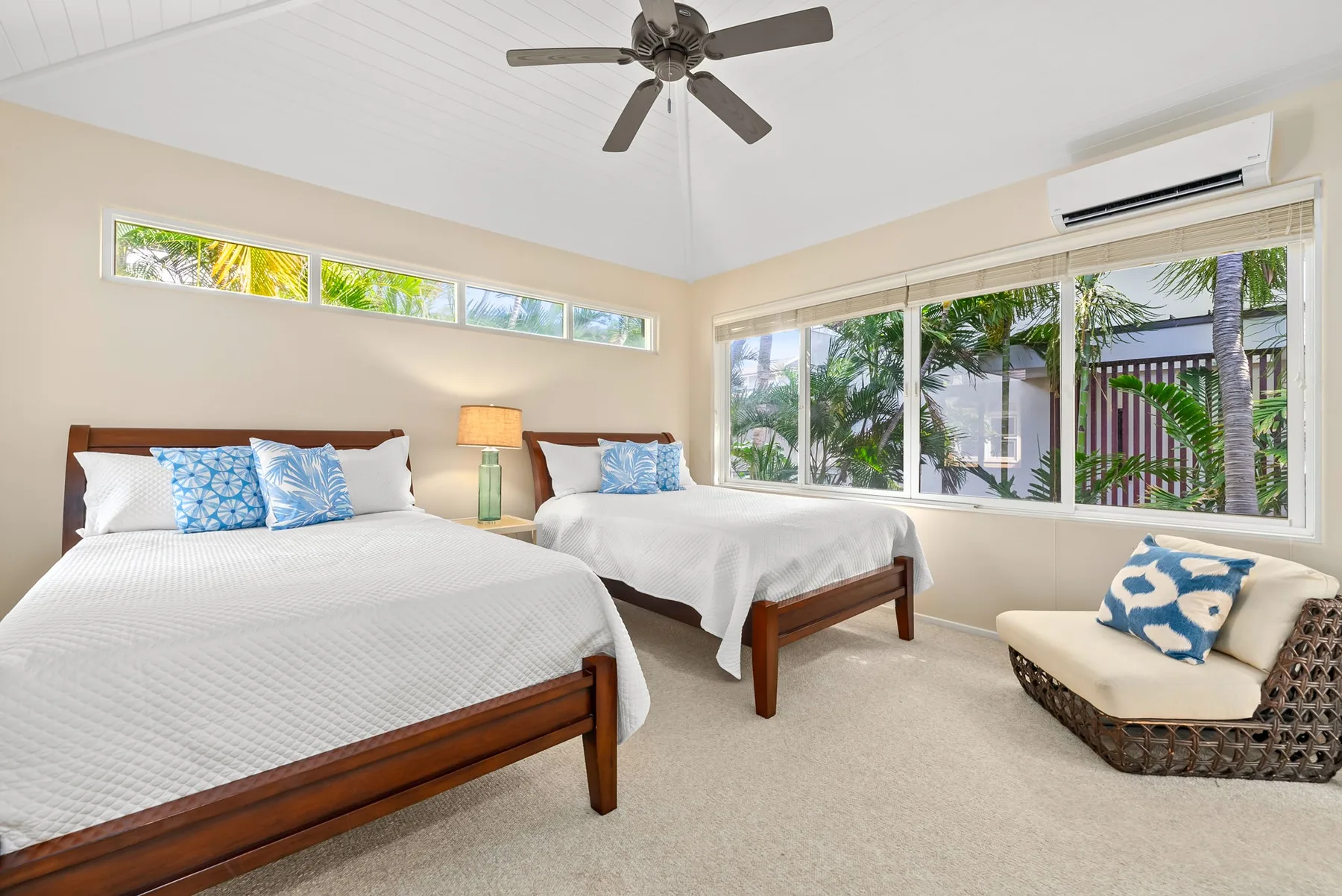 A bright bedroom with two beds and wide windows overlooking greenery.