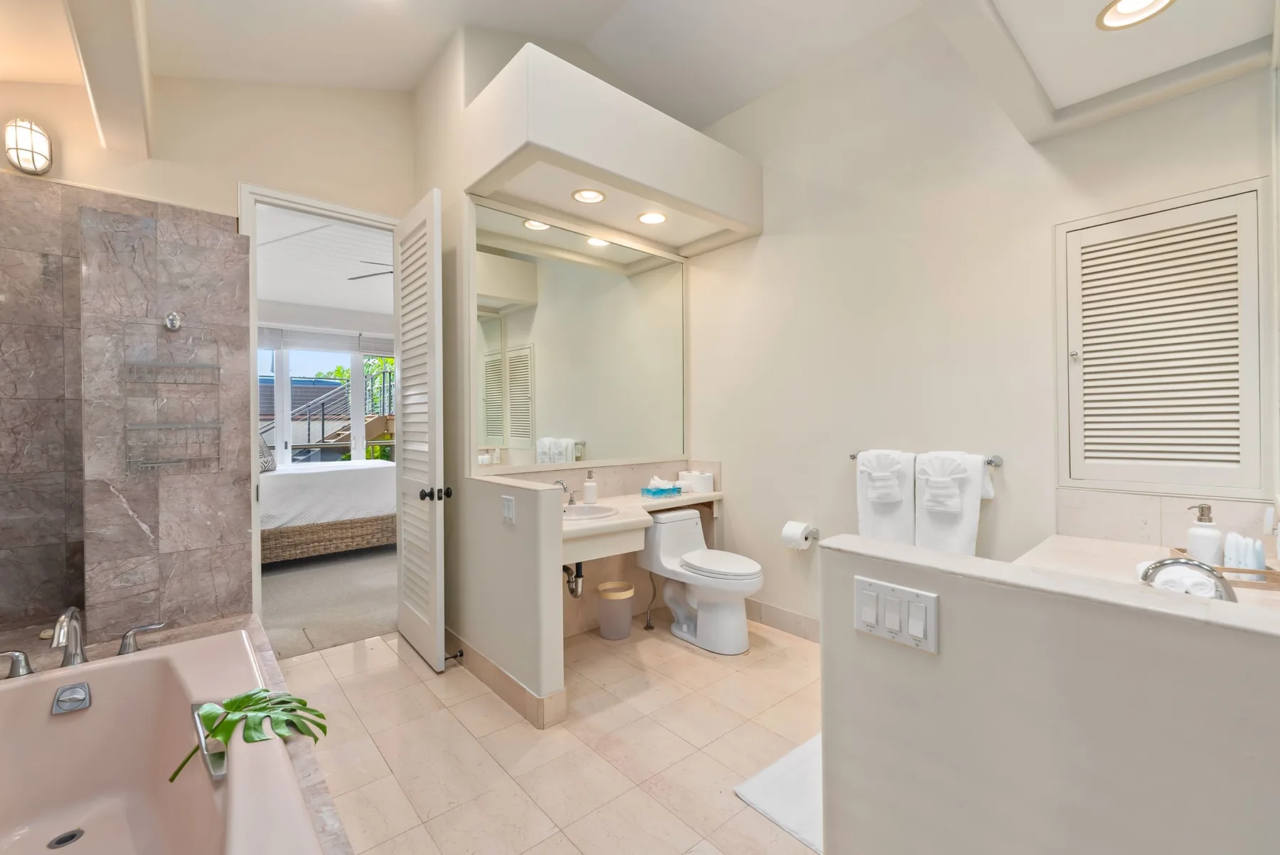 A bright bathroom with a vanity, mirror, toilet, and bathtub.