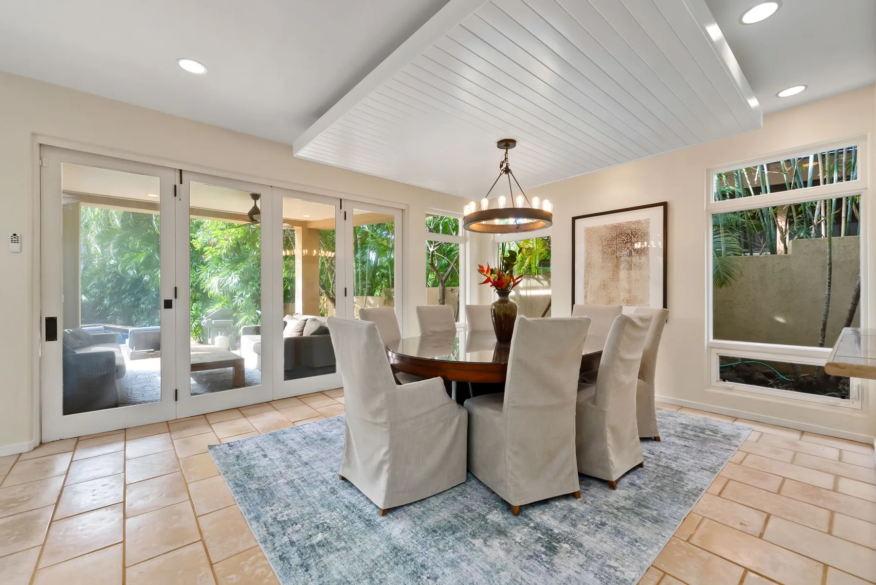 A bright dining room with a table beneath a hanging light and glass doors.