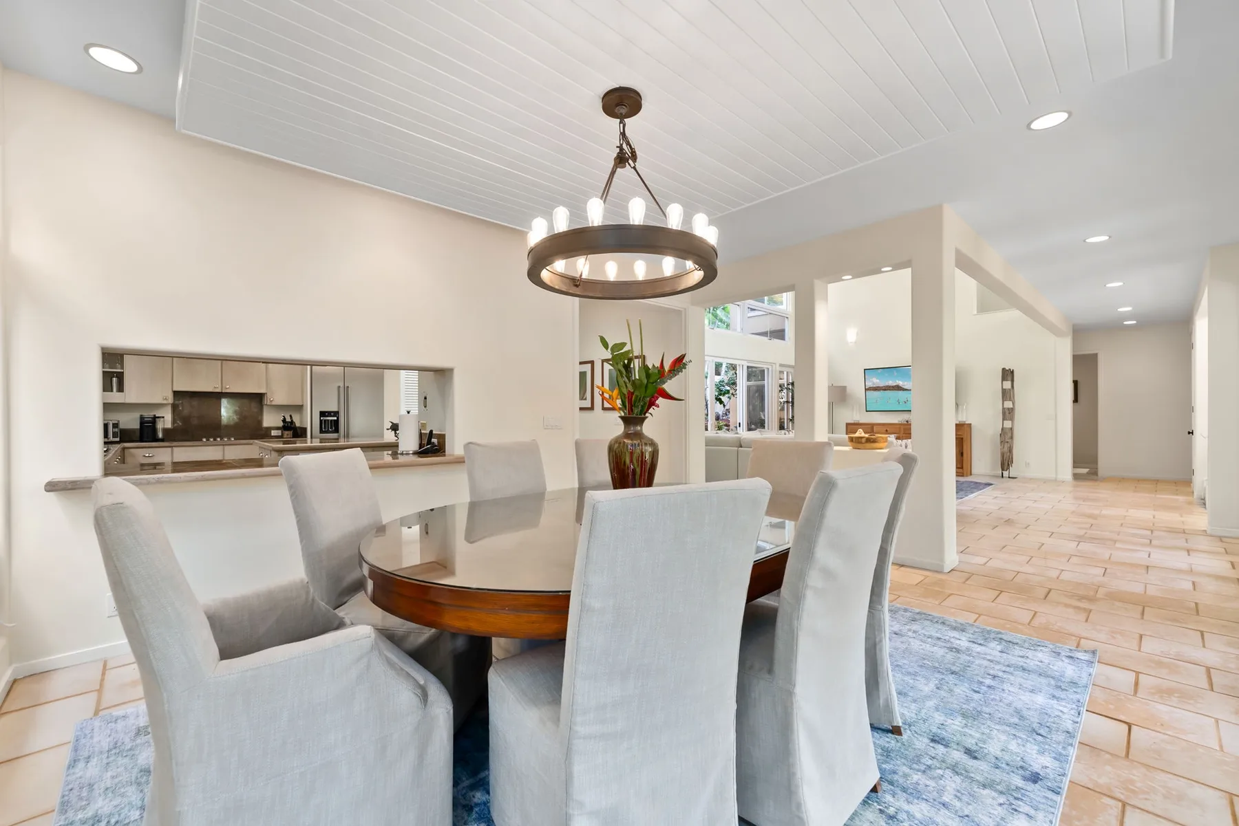 A dining area with upholstered seating around a table and a kitchen in the background.