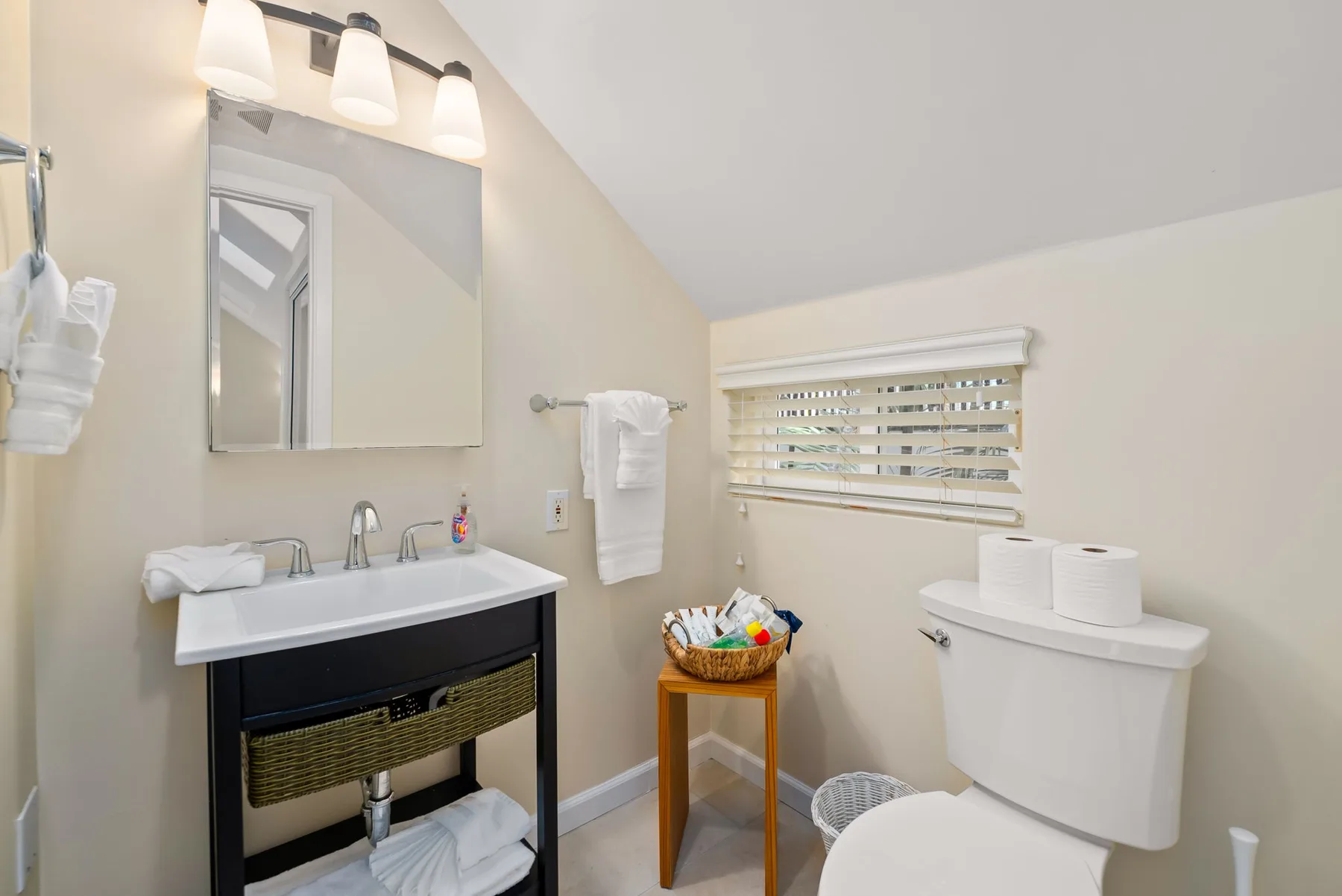 A bright bathroom with a sink, mirror, and toilet beside a window.
