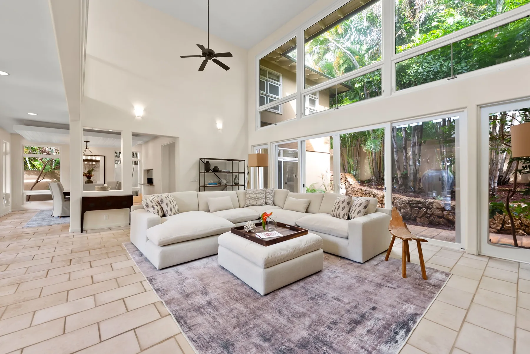 A bright living room with light seating beside tall windows overlooking greenery.