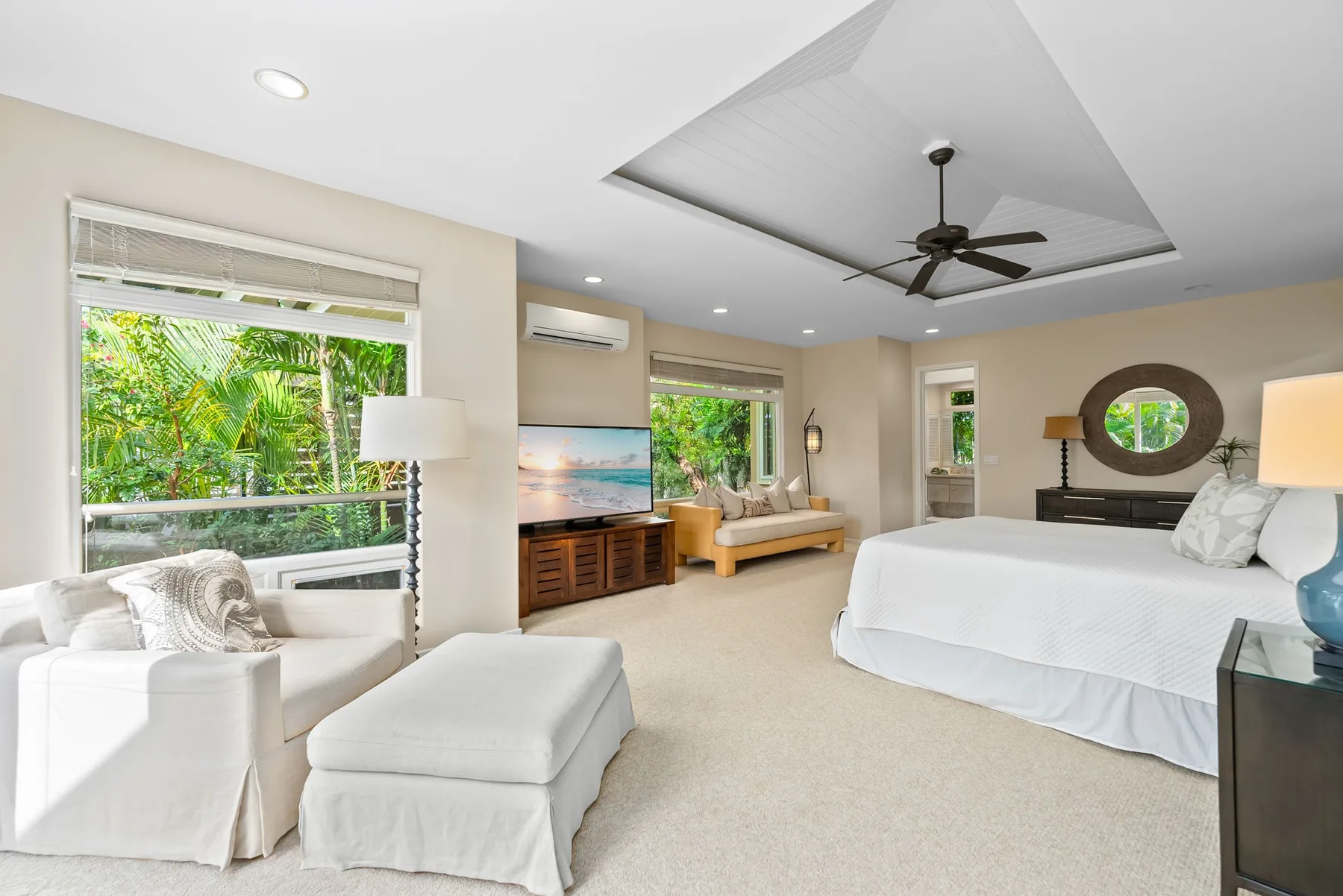 A bright bedroom with a large bed, seating area, and windows overlooking greenery.