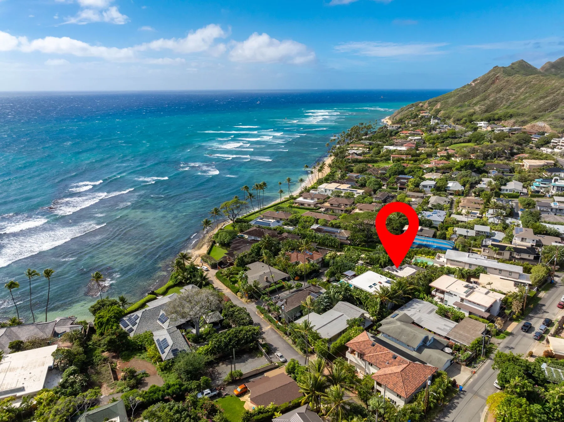Aerial view of a coastal neighborhood beside turquoise water and a green hillside.