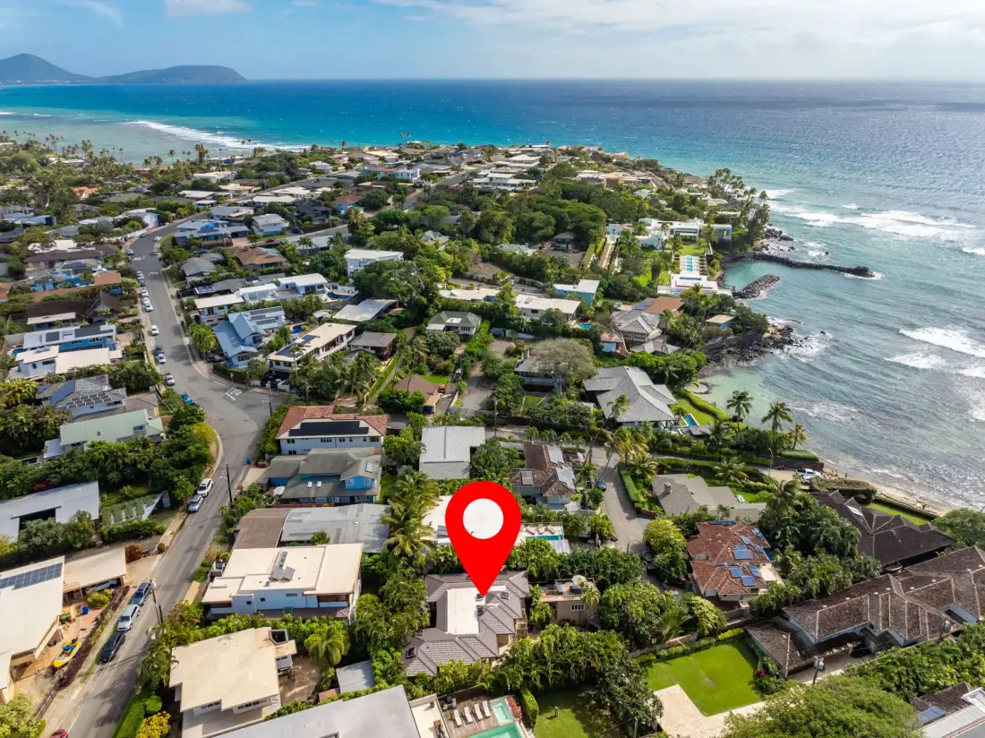Aerial view of a coastal neighborhood with homes, greenery, and ocean shoreline.