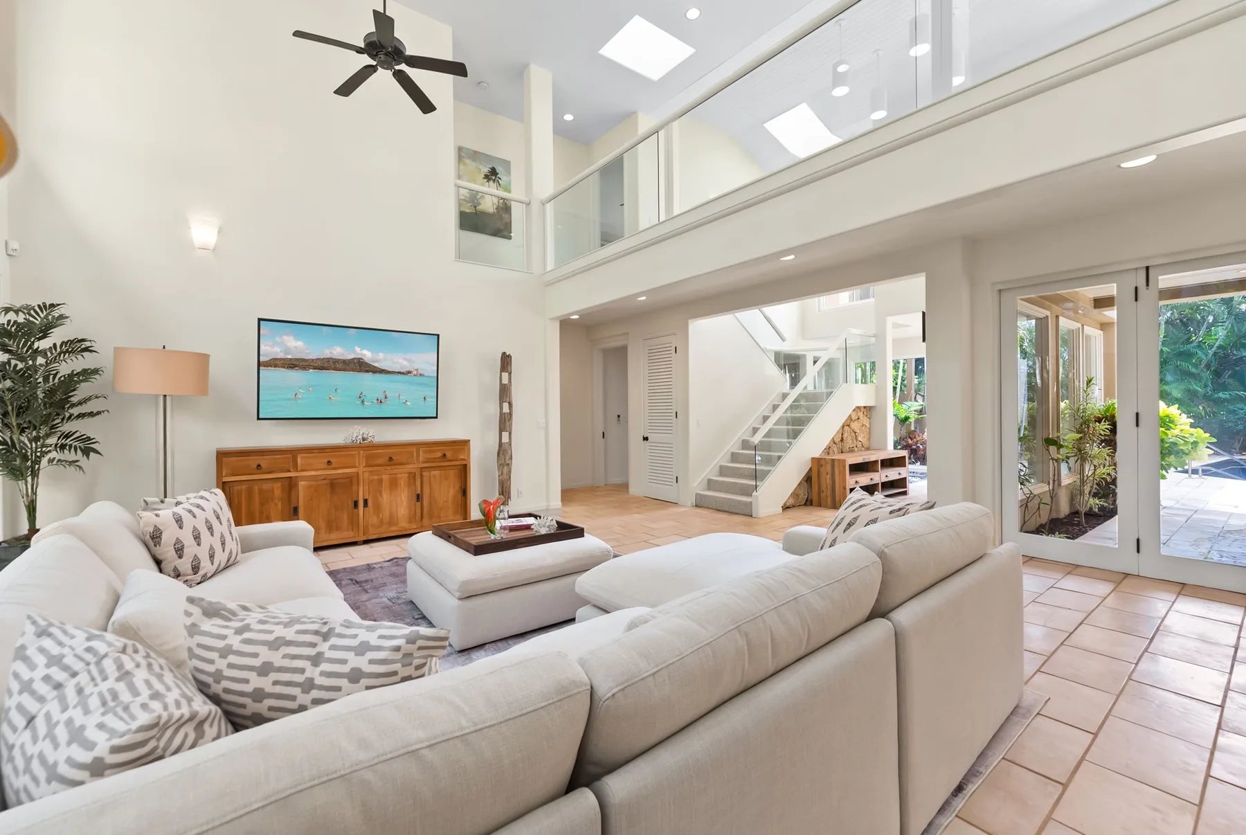 A bright living room with seating, a television, and stairs to an upper level.
