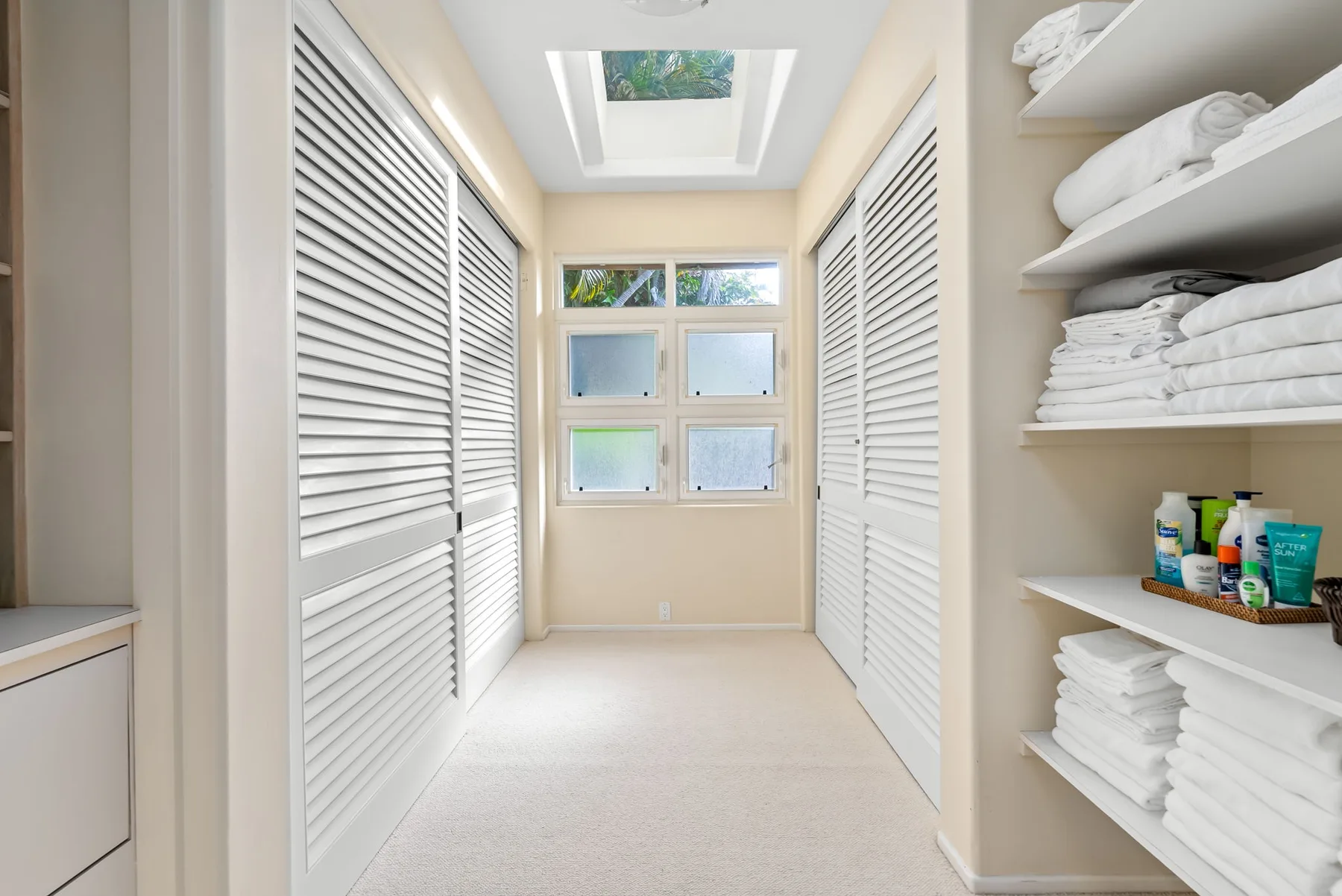 A bright linen storage room with folded towels on open shelves.
