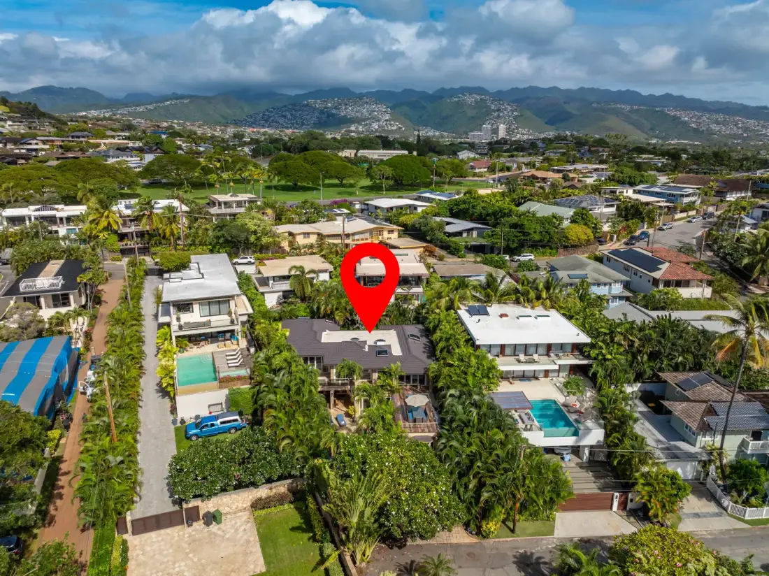An aerial view of homes and green gardens, with mountains in the distance.
