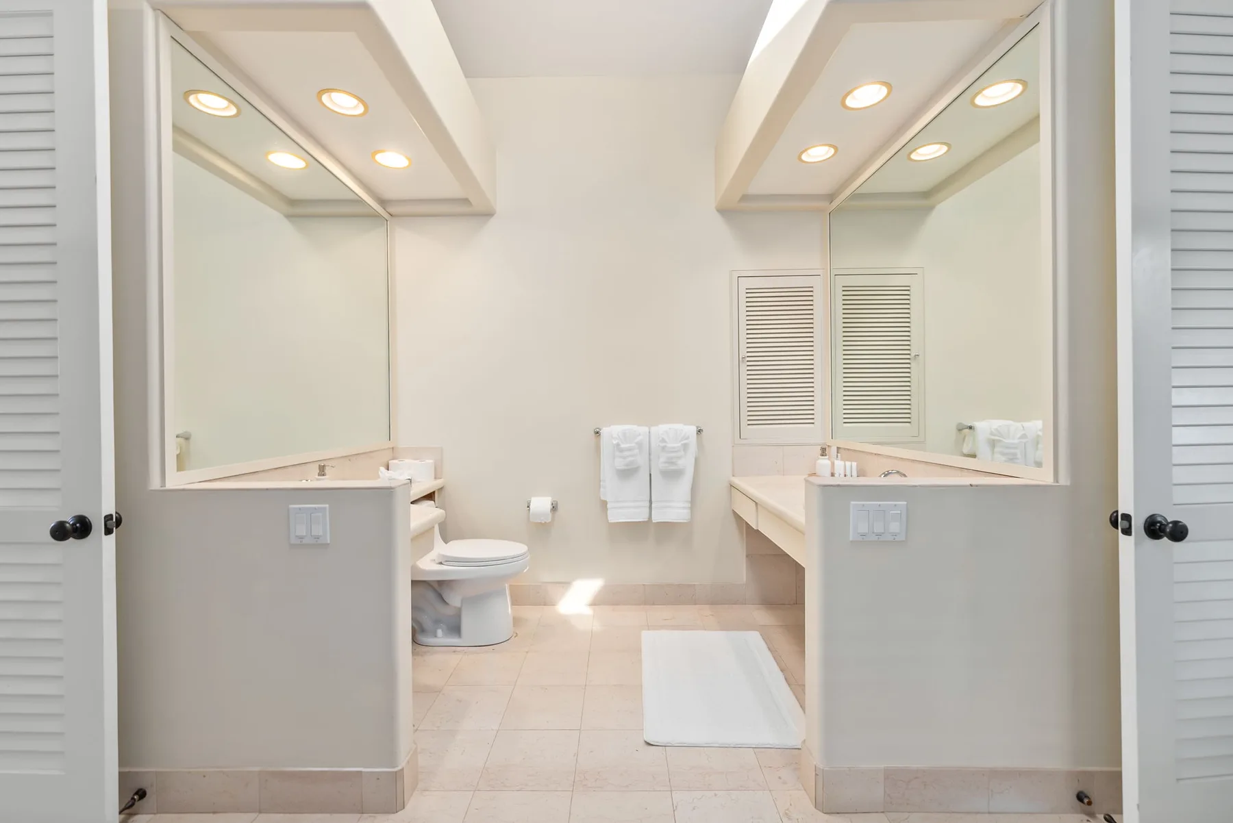 A bright bathroom with mirrored vanity counters and a bathtub.