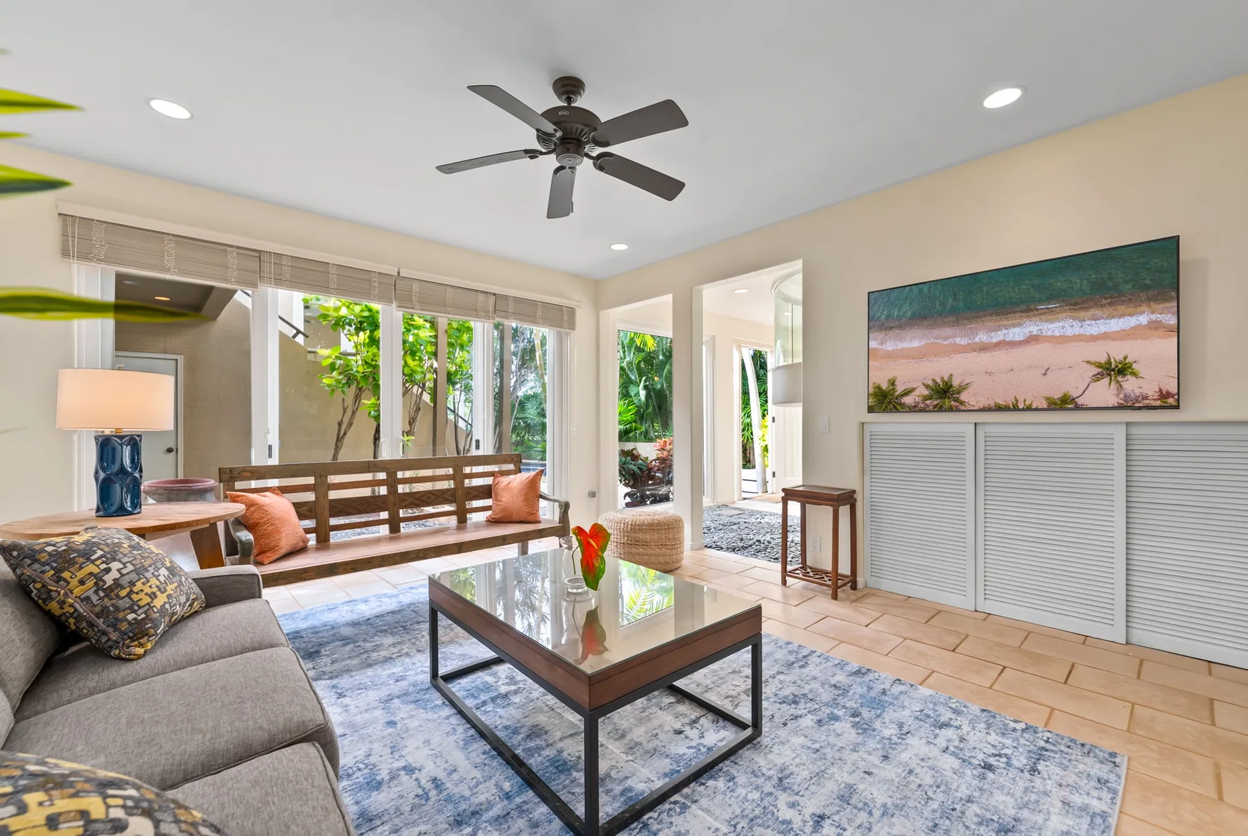 A bright living room with seating, a glass coffee table, and large windows.