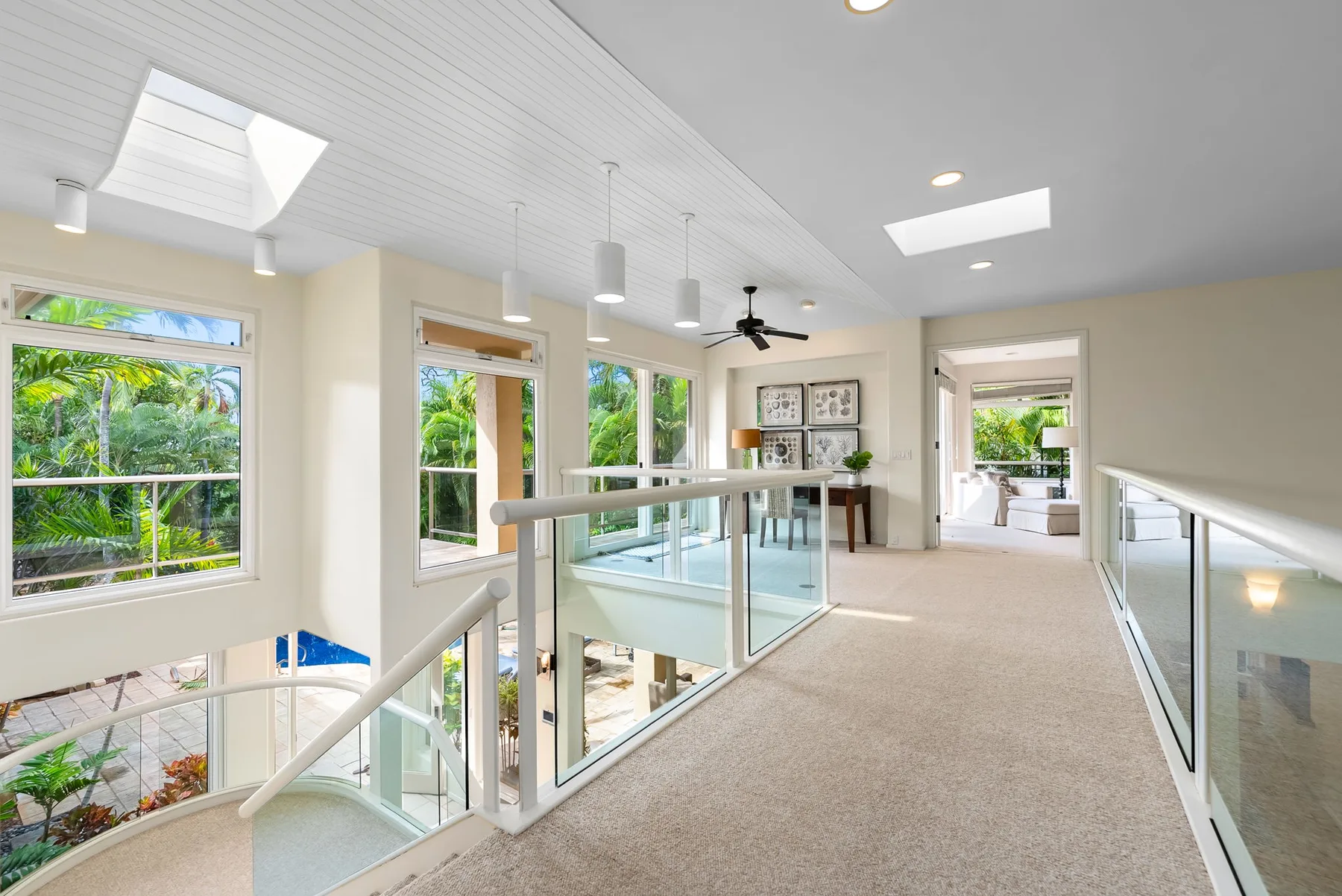A bright upstairs hallway with large windows and glass railings.